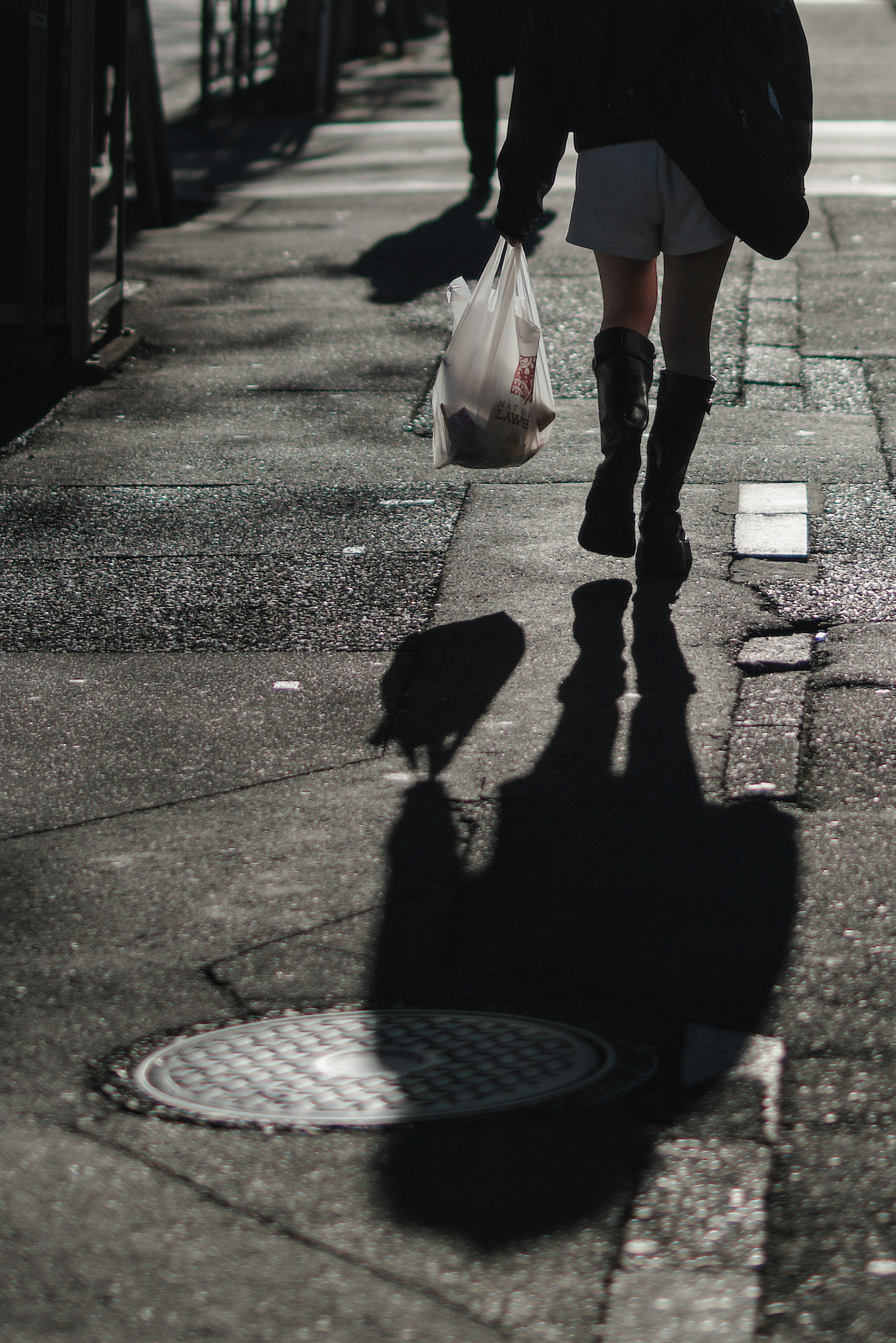 Eine Person, die auf der Straße mit einer Einkaufstüte geht und einen Schatten wirft