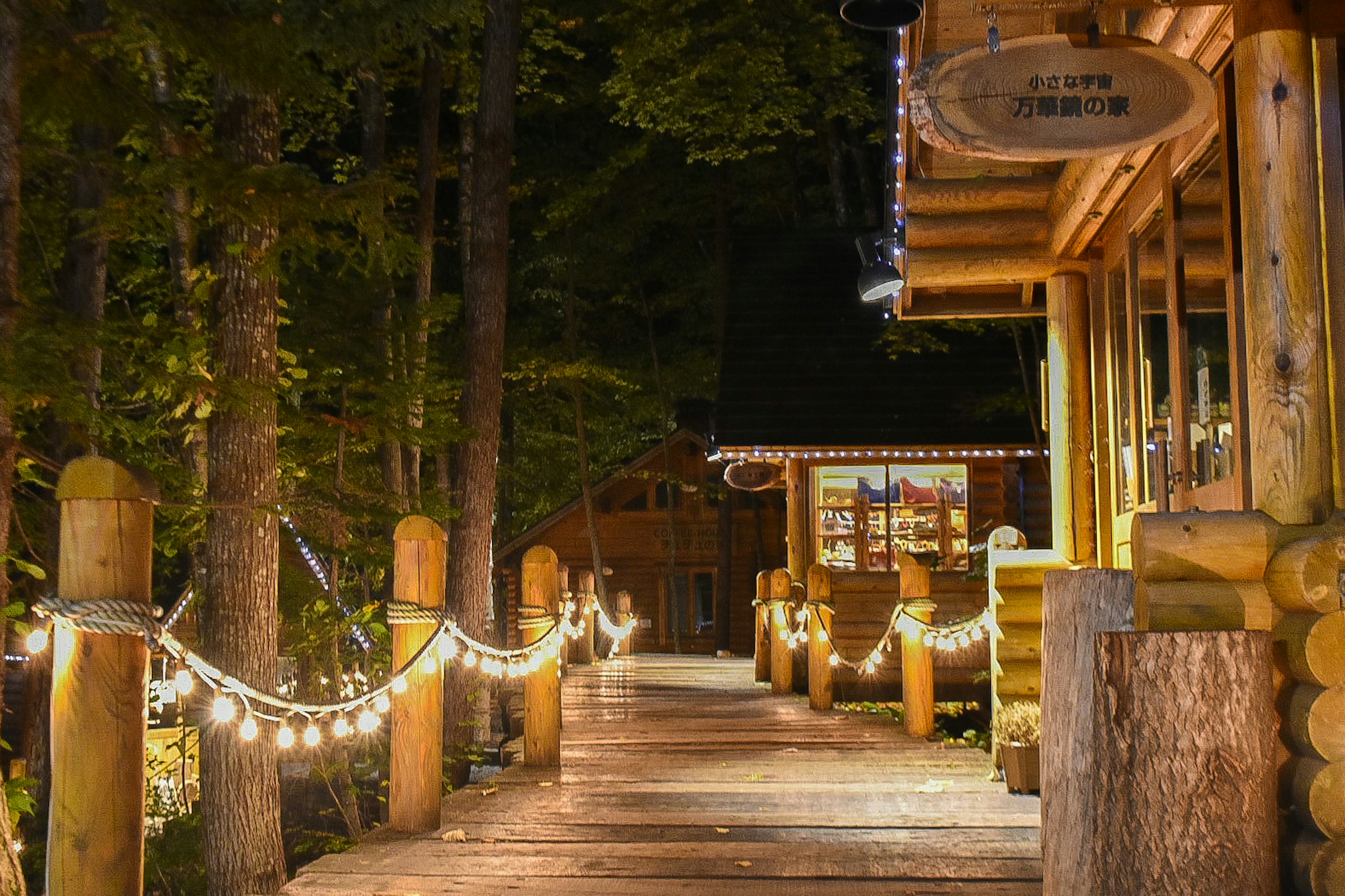 Sentiero in legno illuminato in una foresta di notte con un accogliente chalet