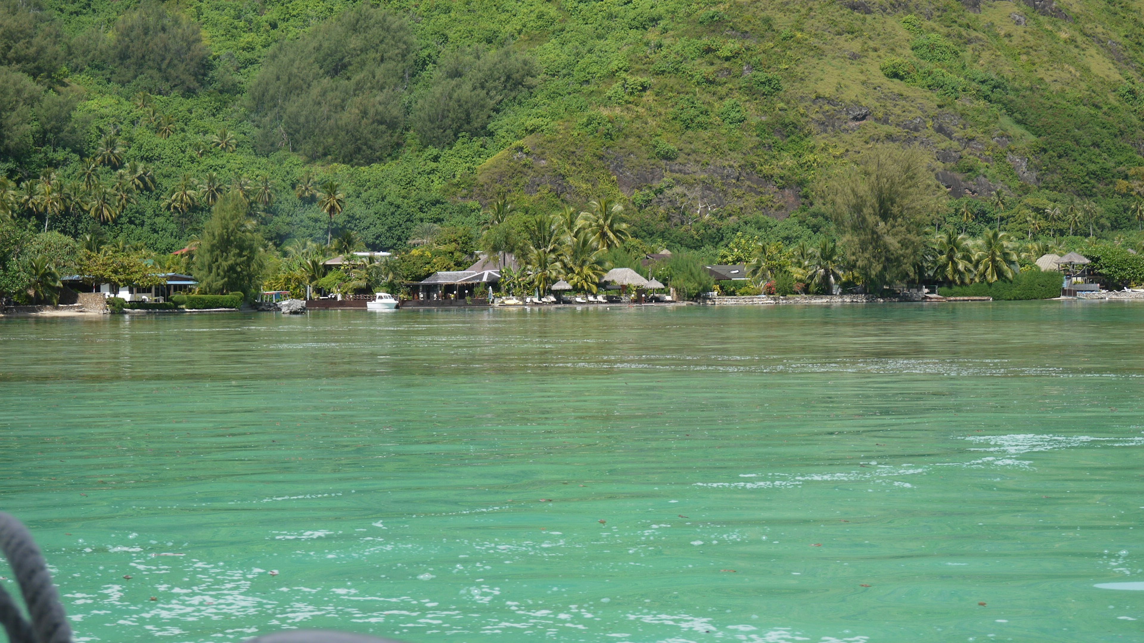 Scenic view of a greenish water surface with lush hills and huts along the shore