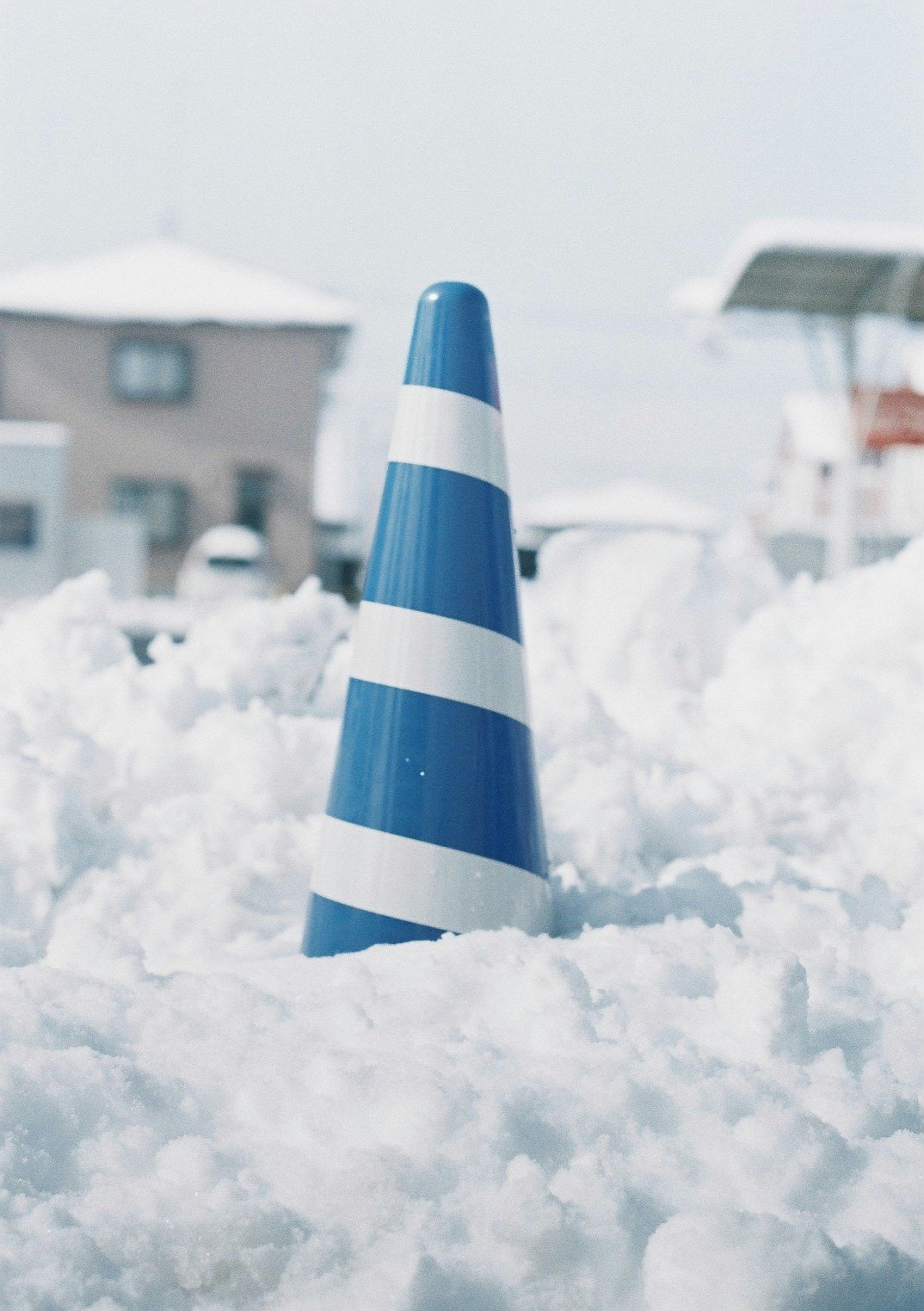 雪に埋もれた青い交通コーンの画像