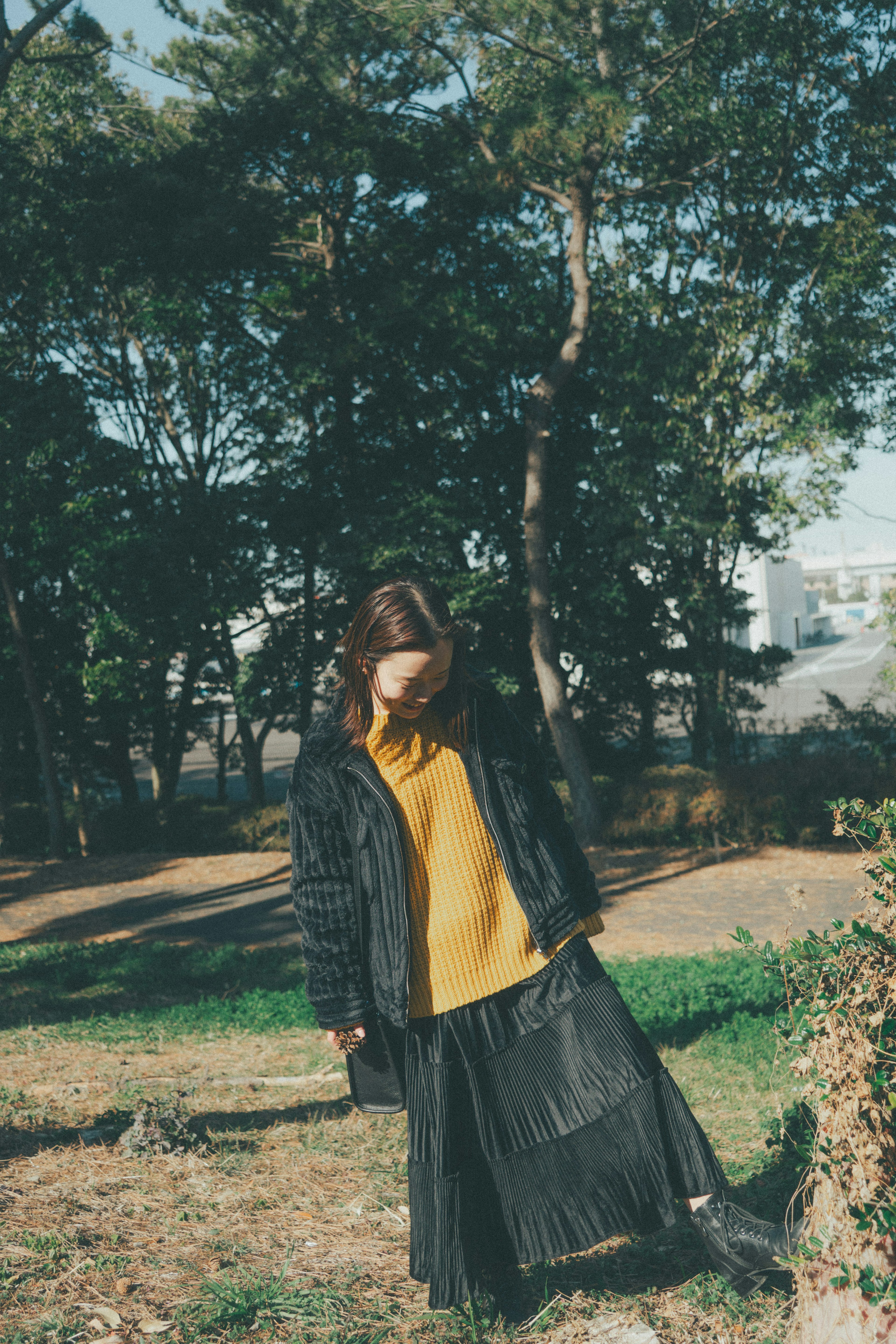 Woman in black coat and yellow sweater standing in a park