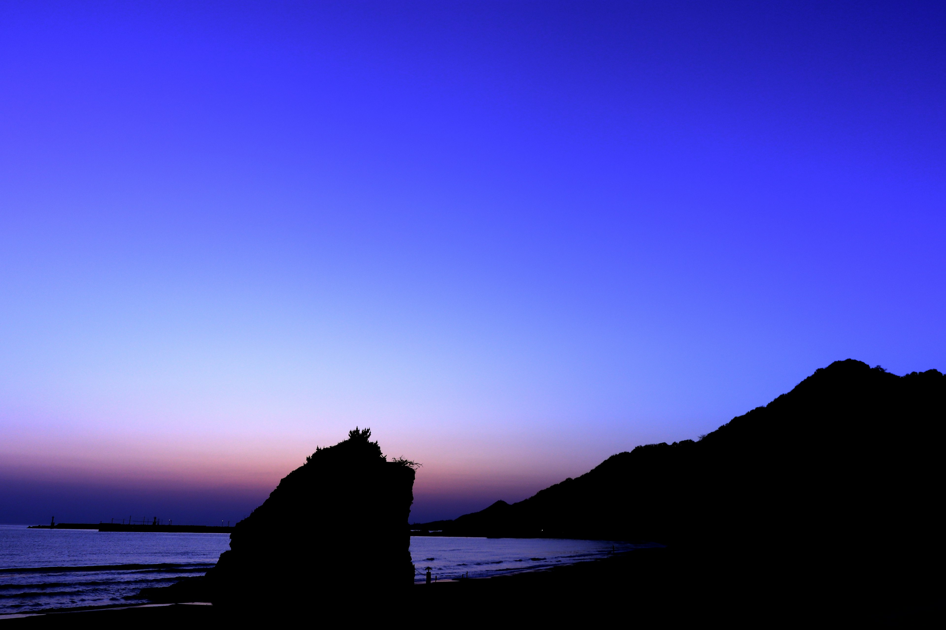 Silhouette eines Felsens und eines Berges bei Dämmerung über dem Meer