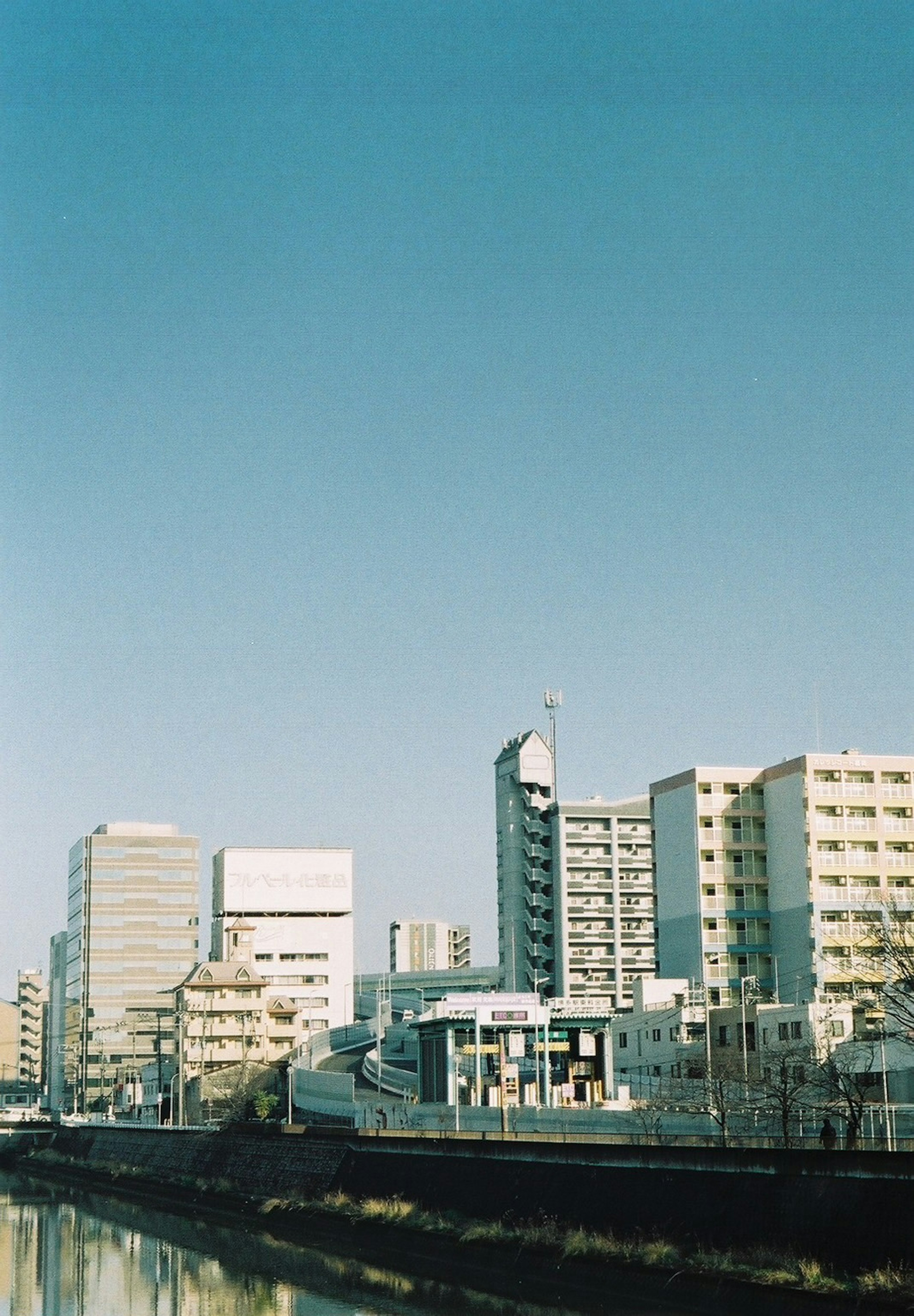 Cityscape featuring tall buildings beside a calm waterway under a clear blue sky