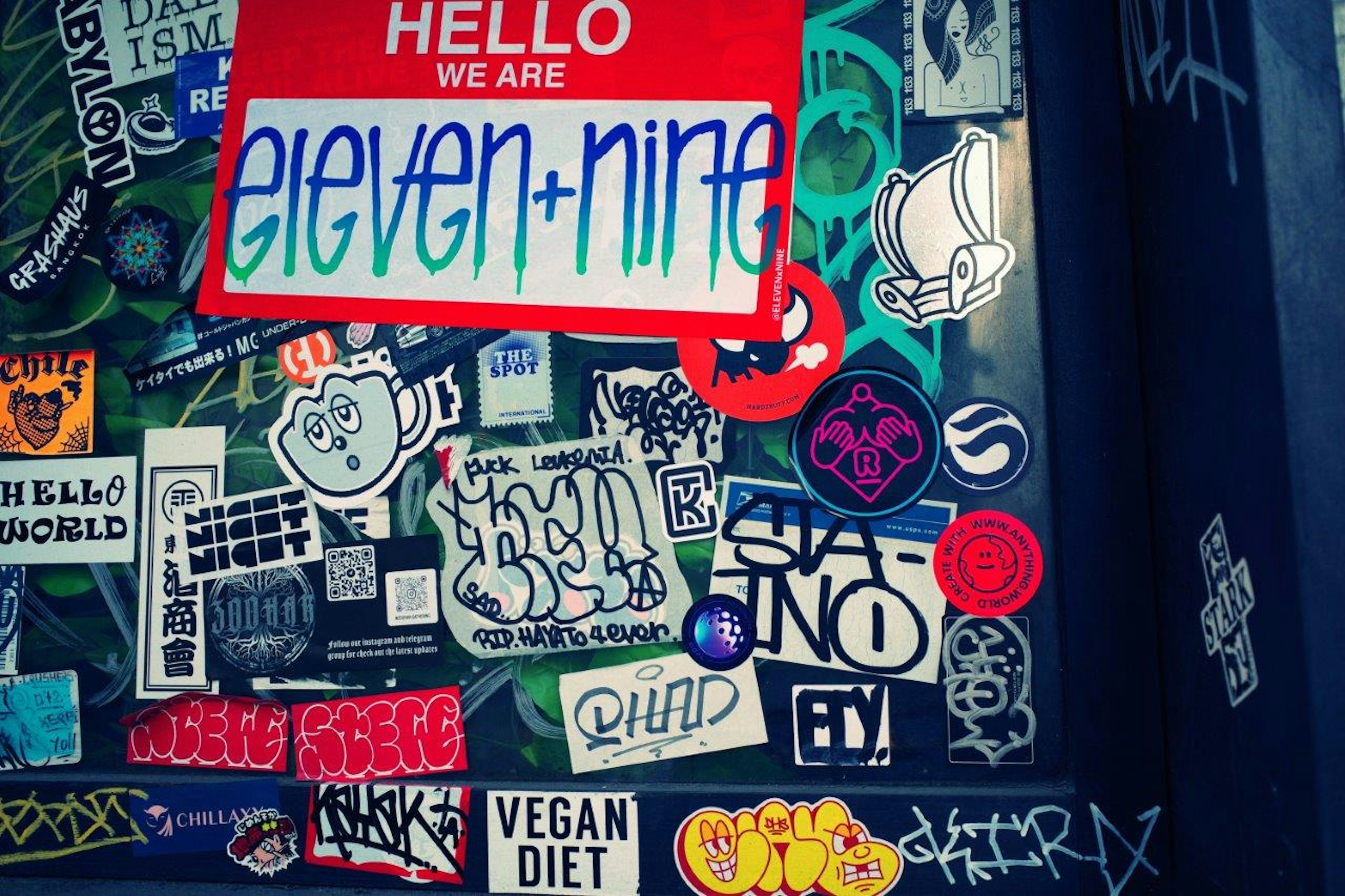 Pegatinas coloridas en una pared con el mensaje 'HELLO WE ARE eleven+nine' destacado