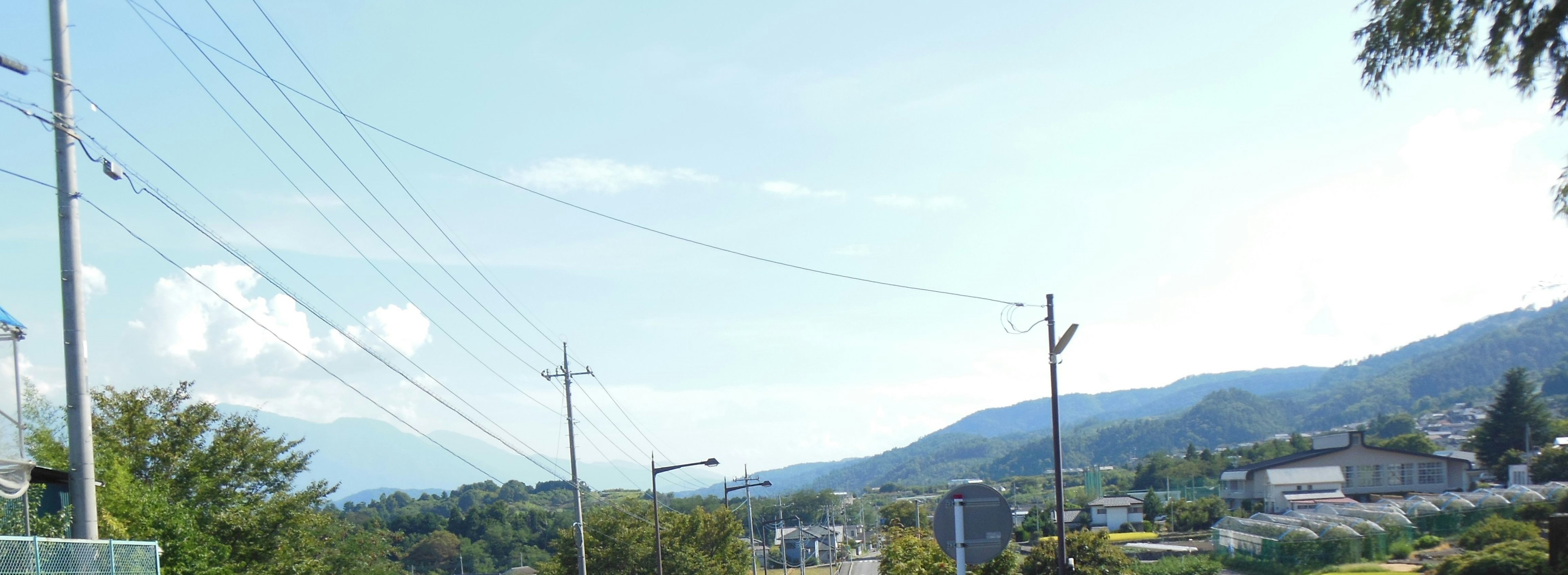 Jalan pedesaan dengan tiang listrik di bawah langit biru cerah dan pegunungan di latar belakang