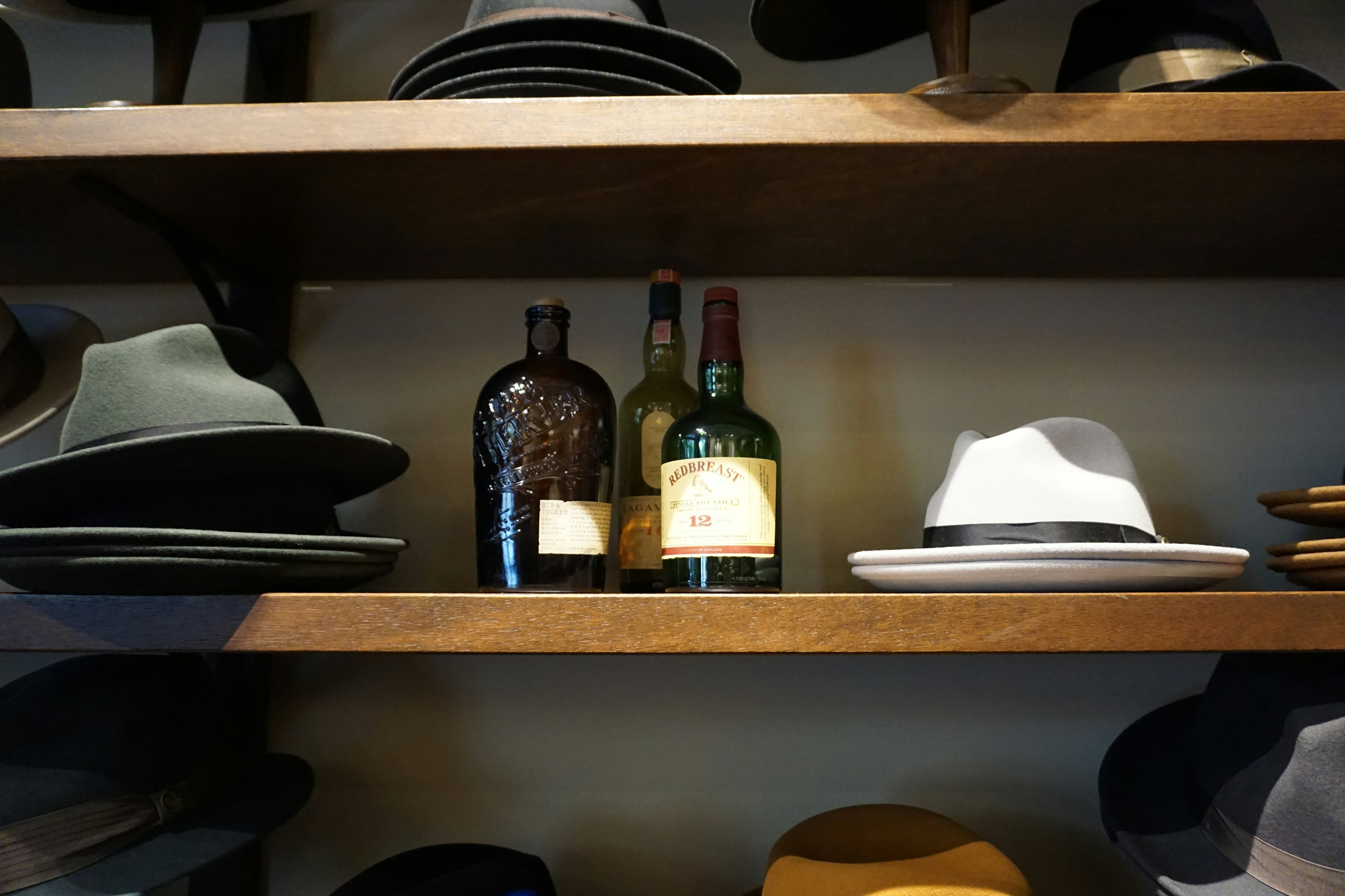 Foto de una estantería de madera con varios sombreros y botellas