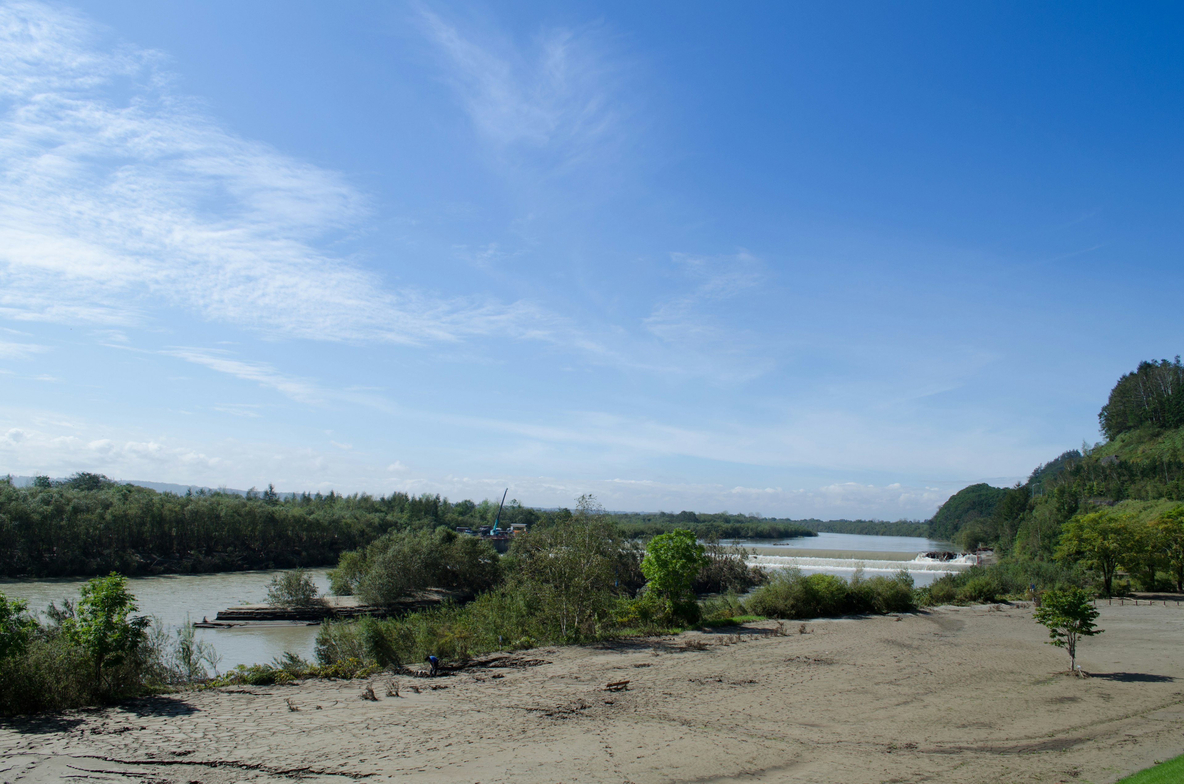 Vista panoramica di un fiume sotto un cielo blu con terreno sabbioso e vegetazione