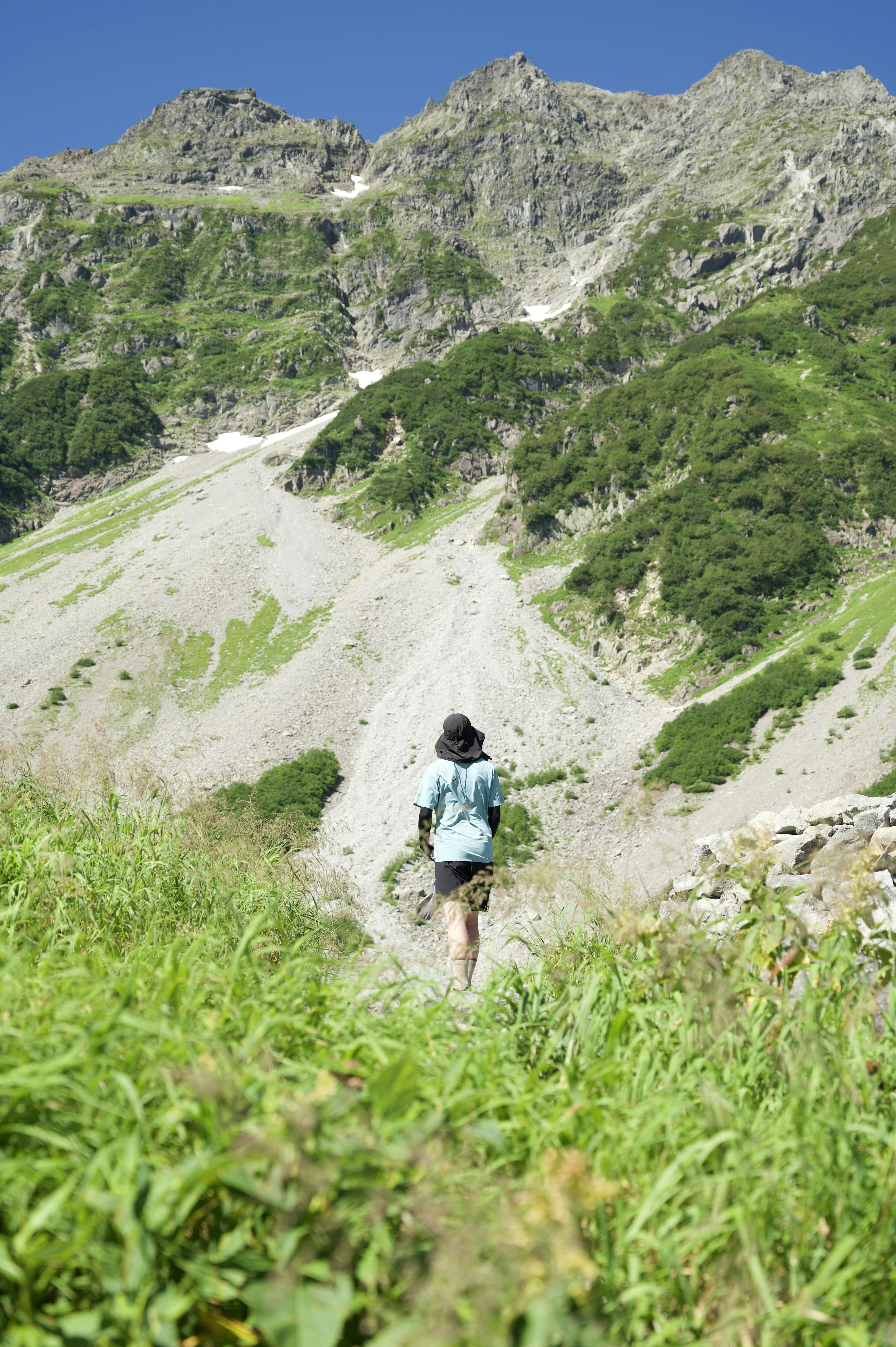 女人在山路上行走，周圍是綠色的草和岩石地形