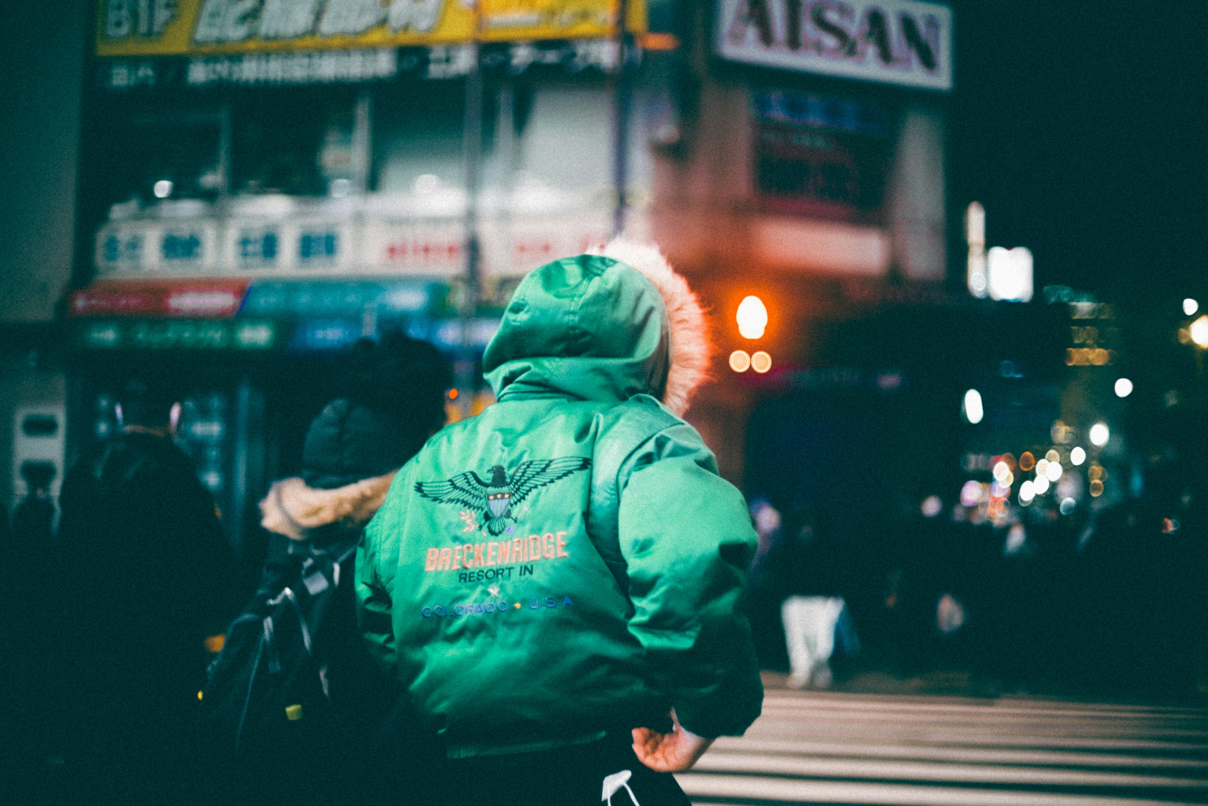 Person wearing a green jacket walking in a city at night