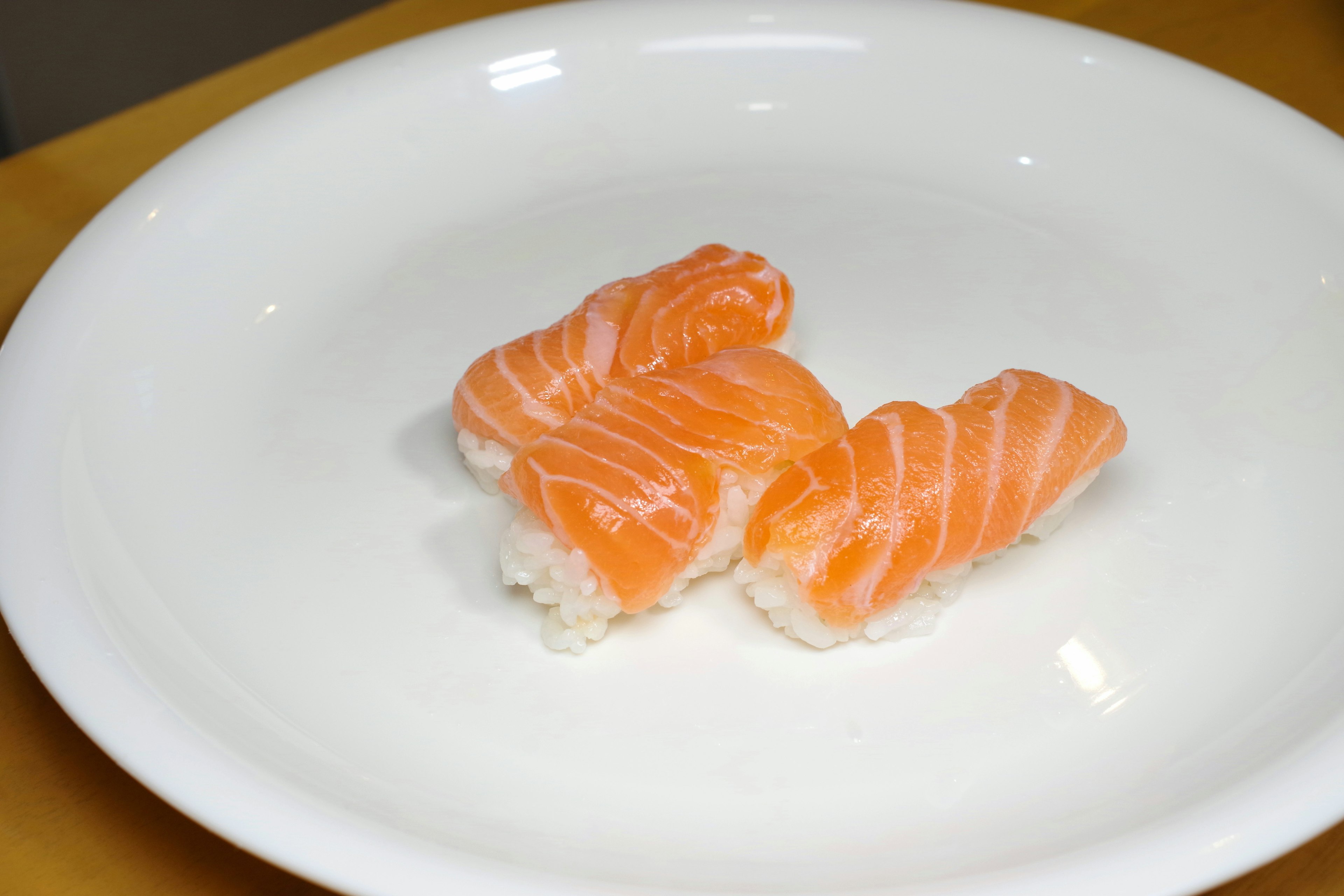 Tre pezzi di sushi nigiri al salmone su un piatto bianco