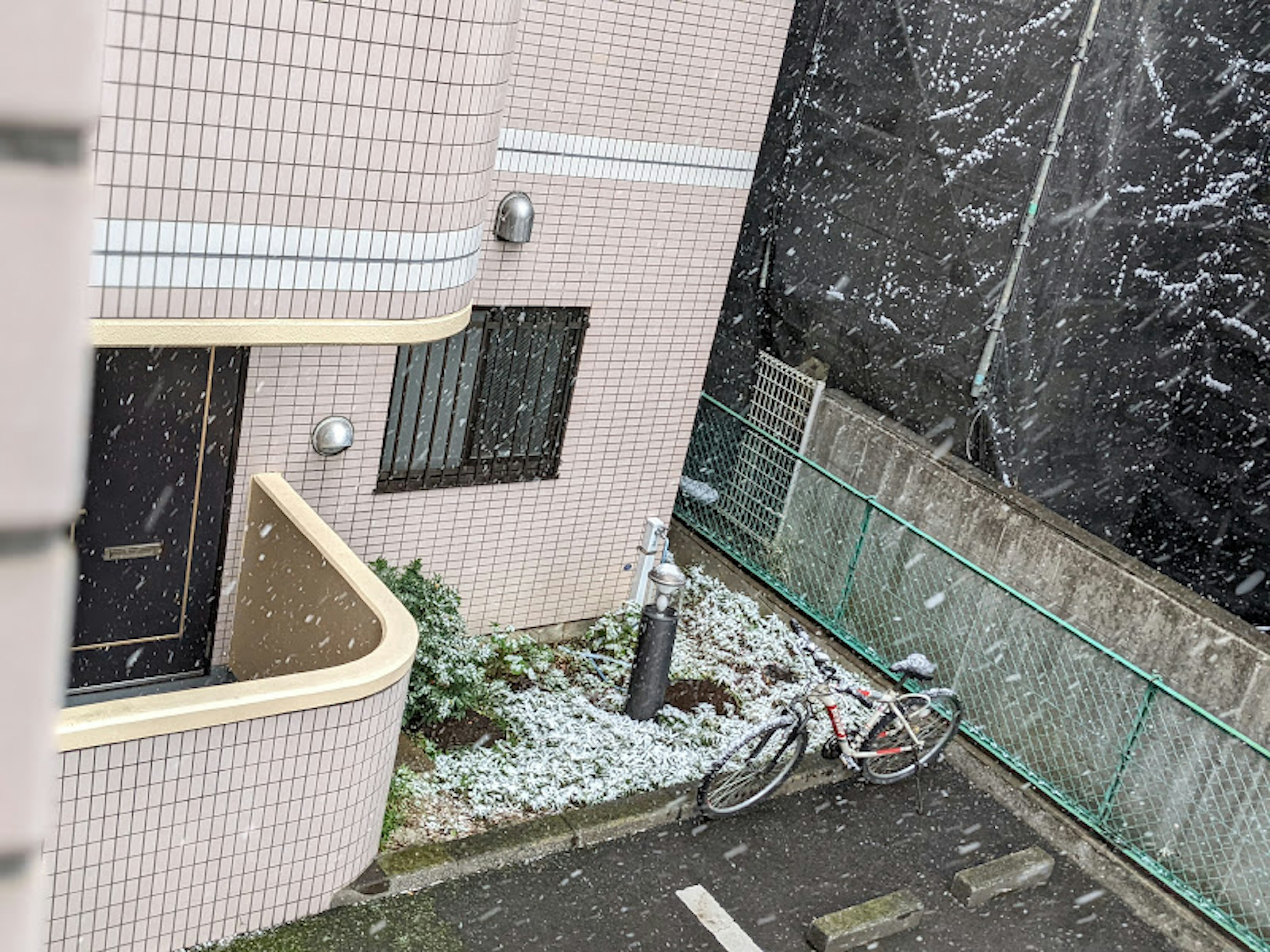 Pink building with snow falling and a bicycle in the courtyard