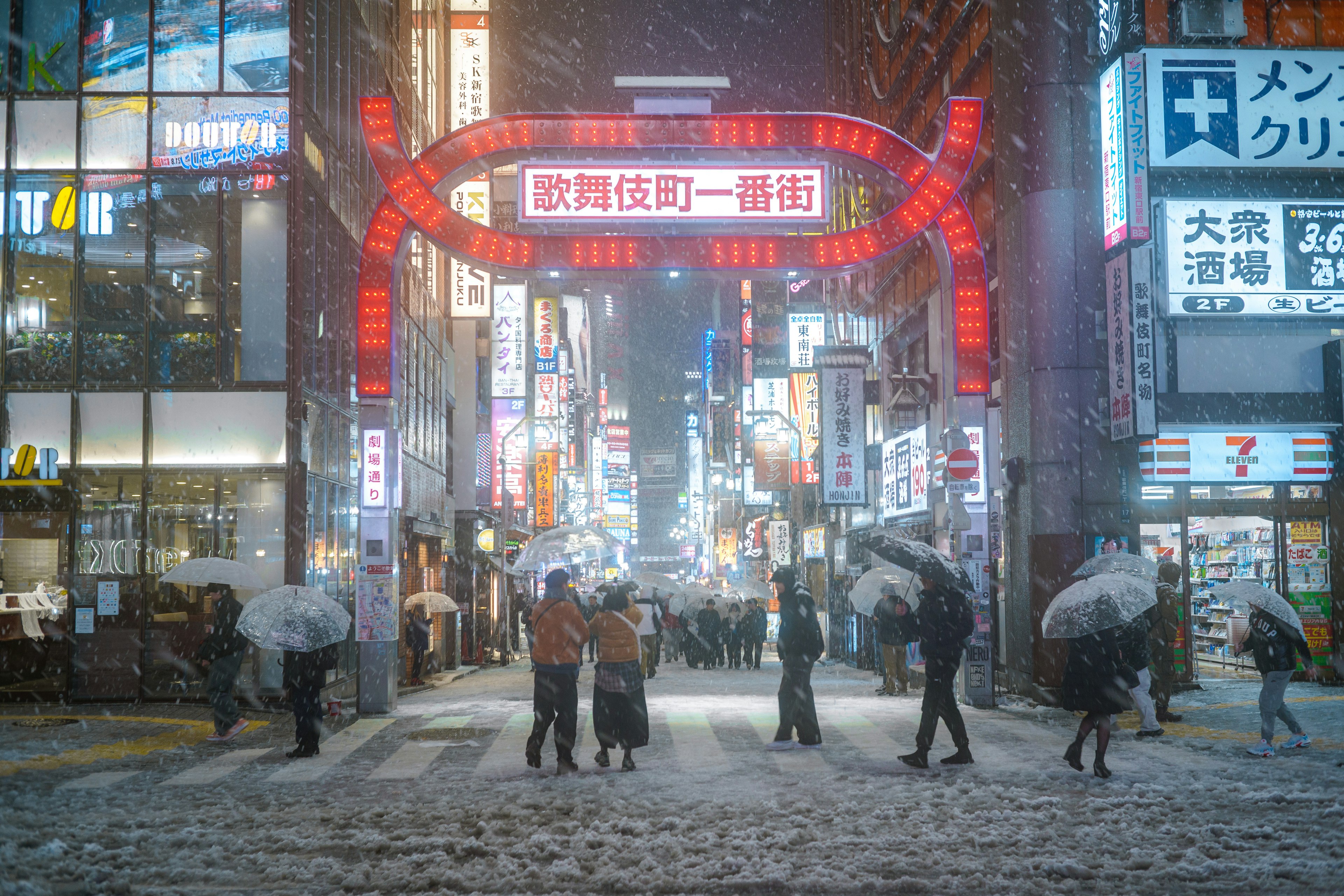 雪の降る夜の繁華街にあるネオンの看板と傘を持つ人々