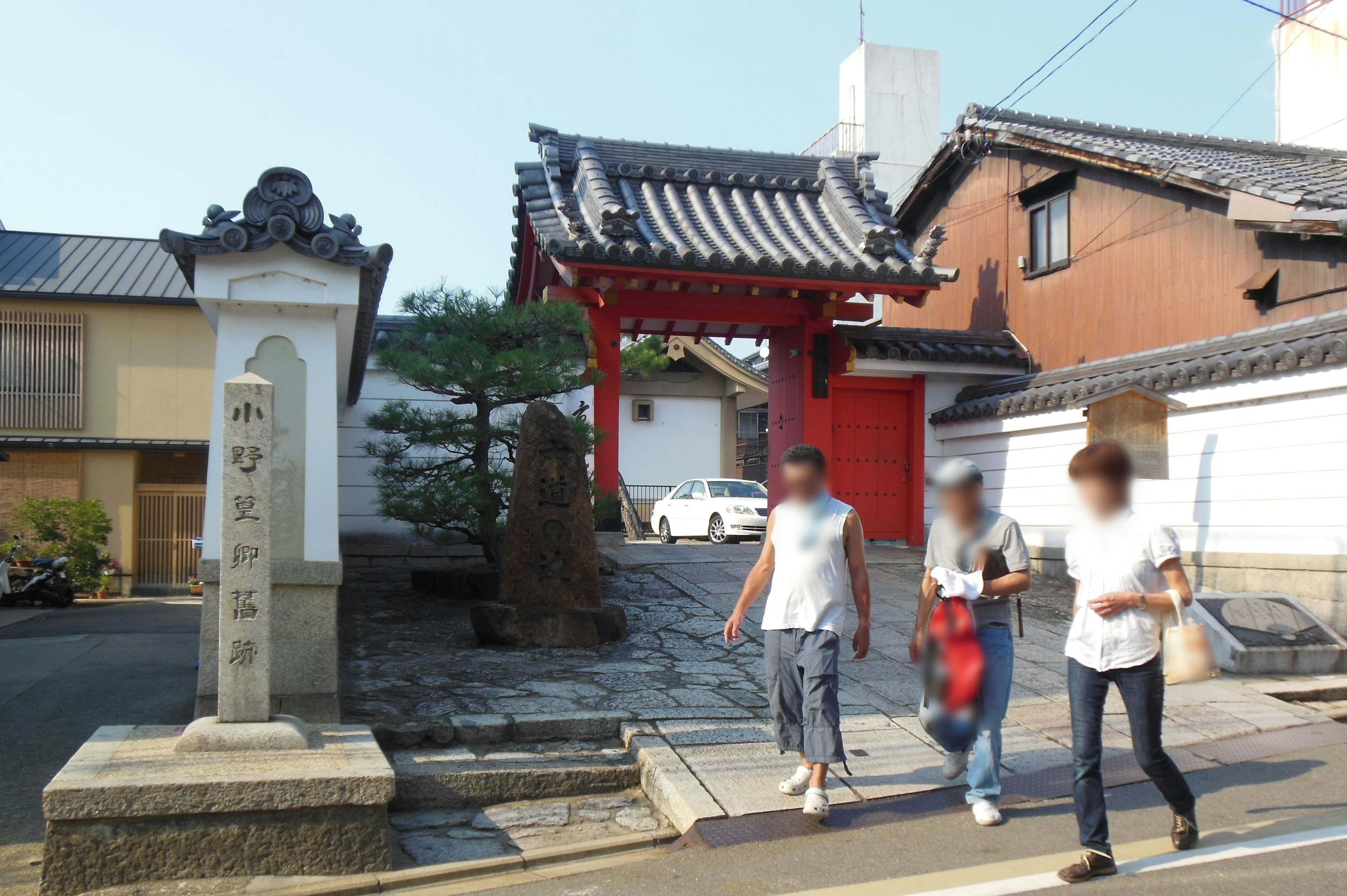 Personas caminando en una calle japonesa tradicional con una puerta roja y un monumento de piedra