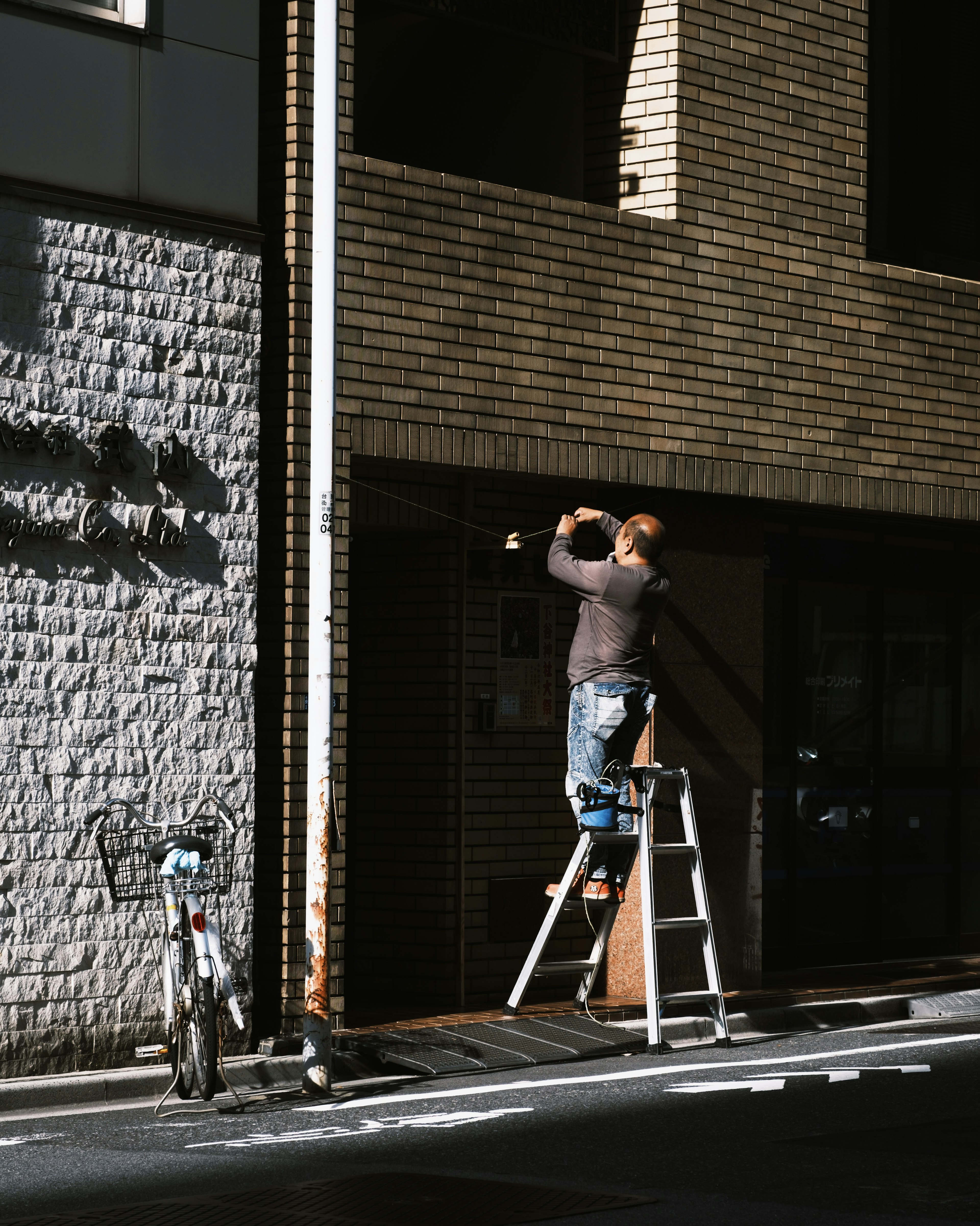 Man working on a brown brick building using a ladder bicycle nearby