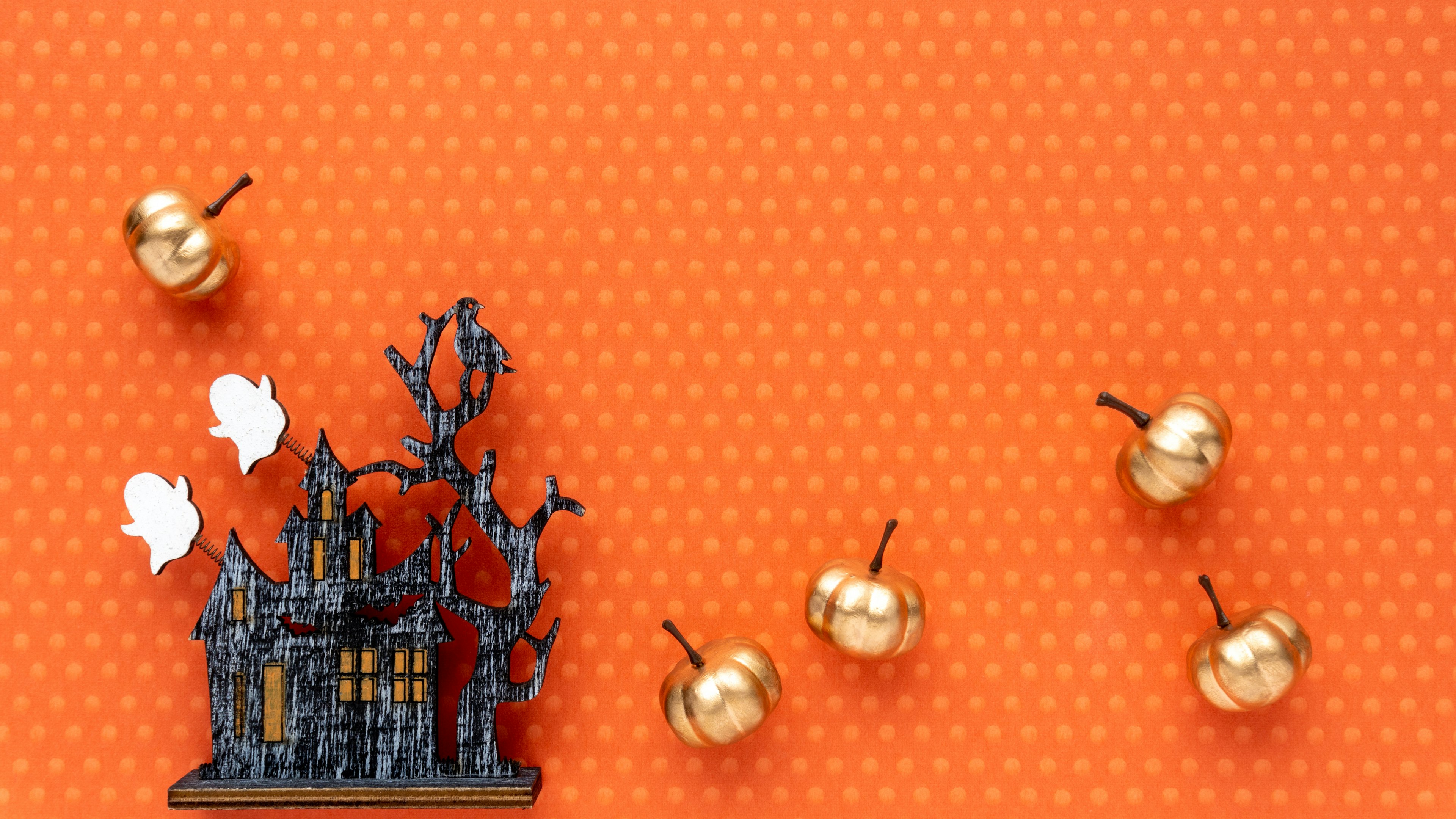 A spooky black haunted house and golden pumpkins on an orange background