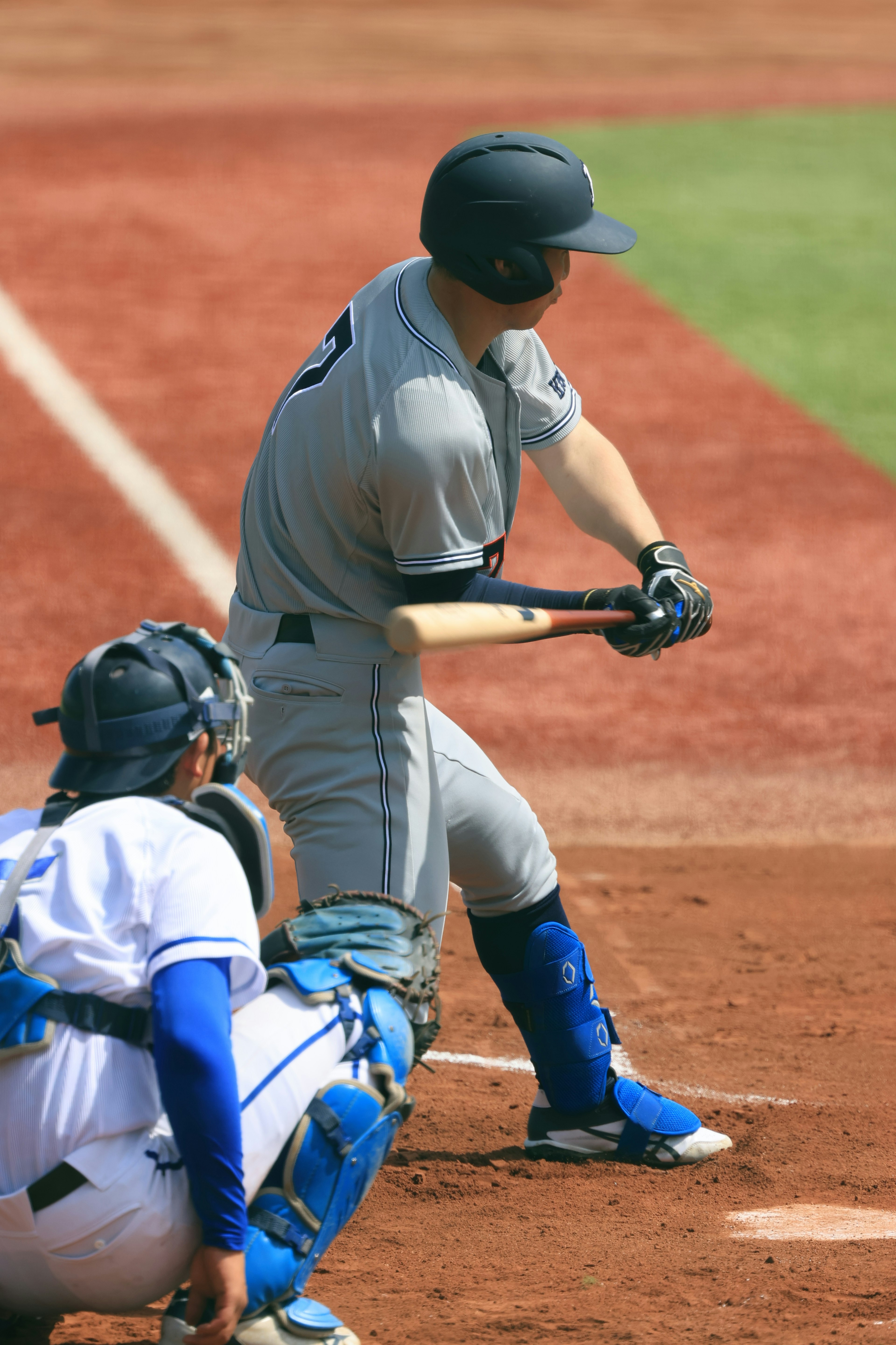 Baseball player swinging a bat with a catcher in the background