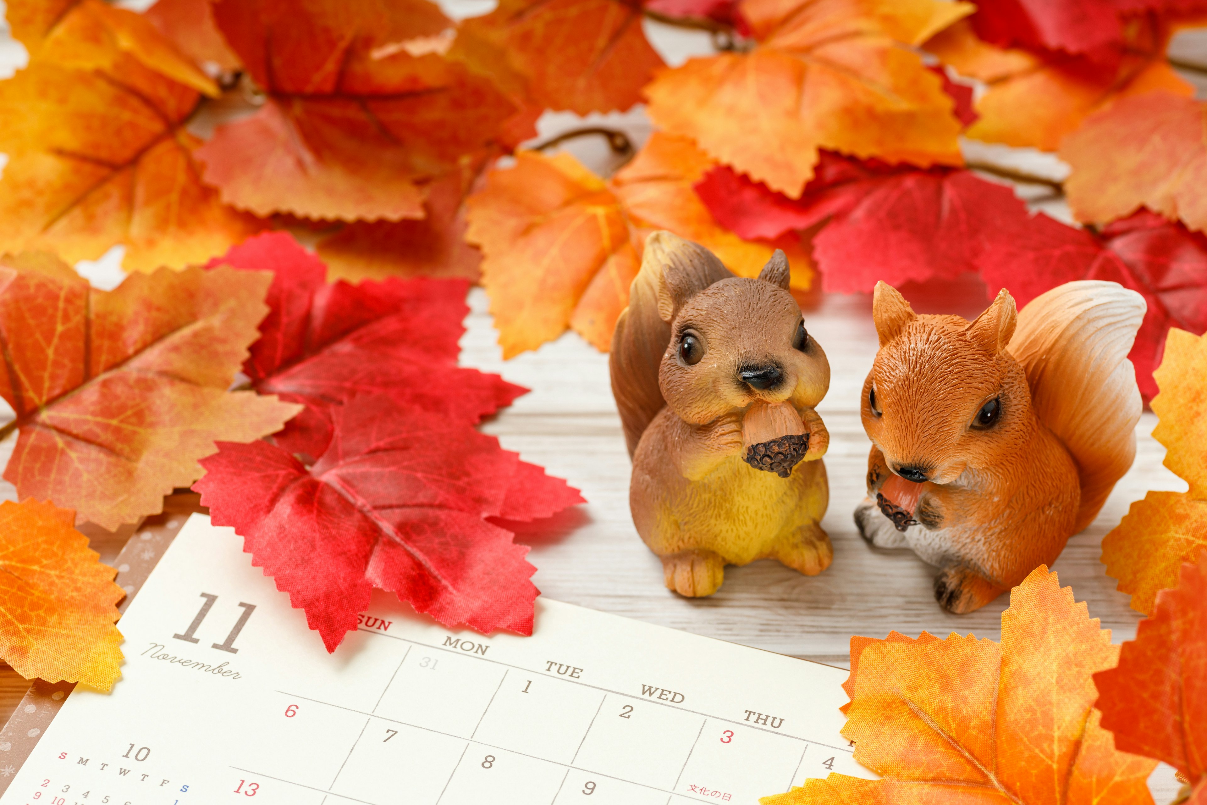 Two squirrel figurines among autumn leaves with a calendar