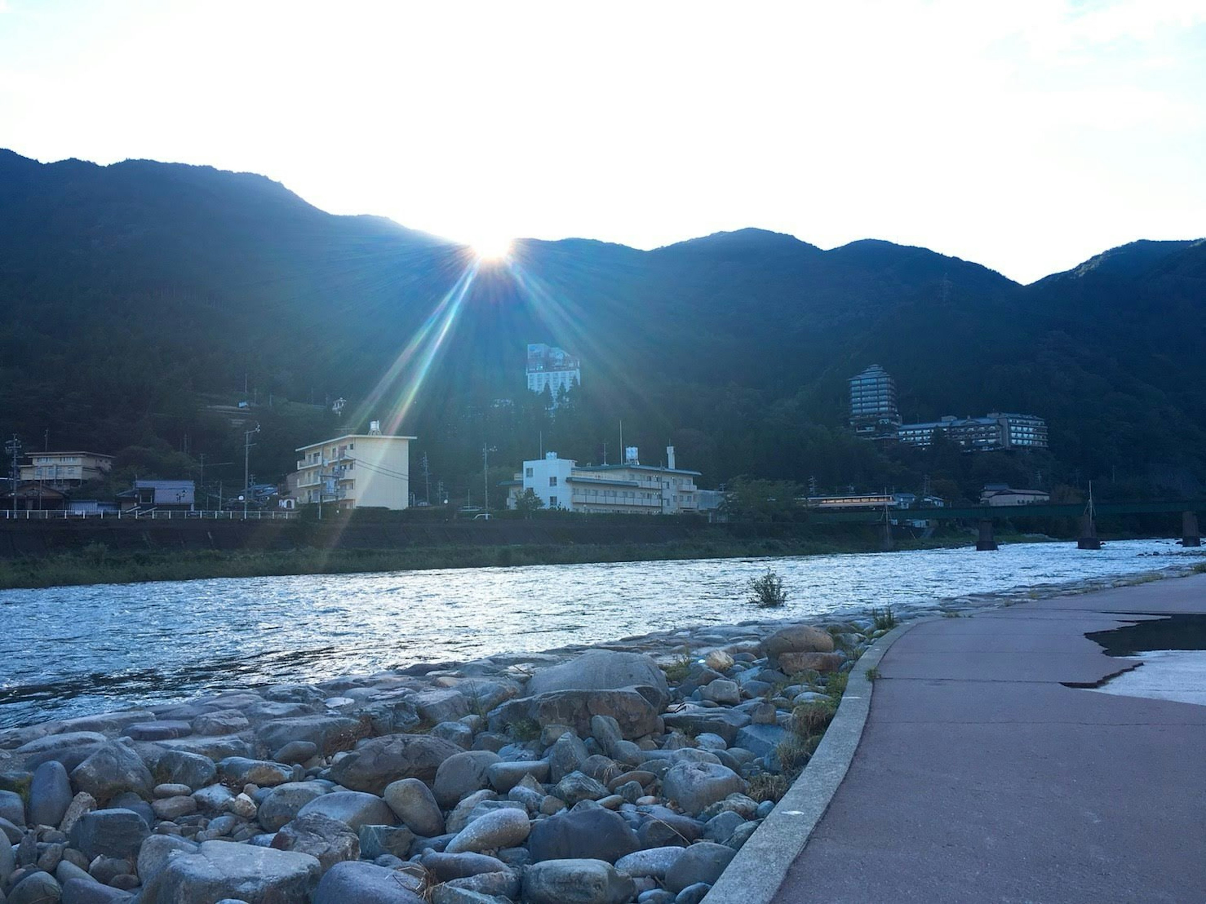 Sonnenlicht, das zwischen Bergen entlang eines Uferwegs strömt