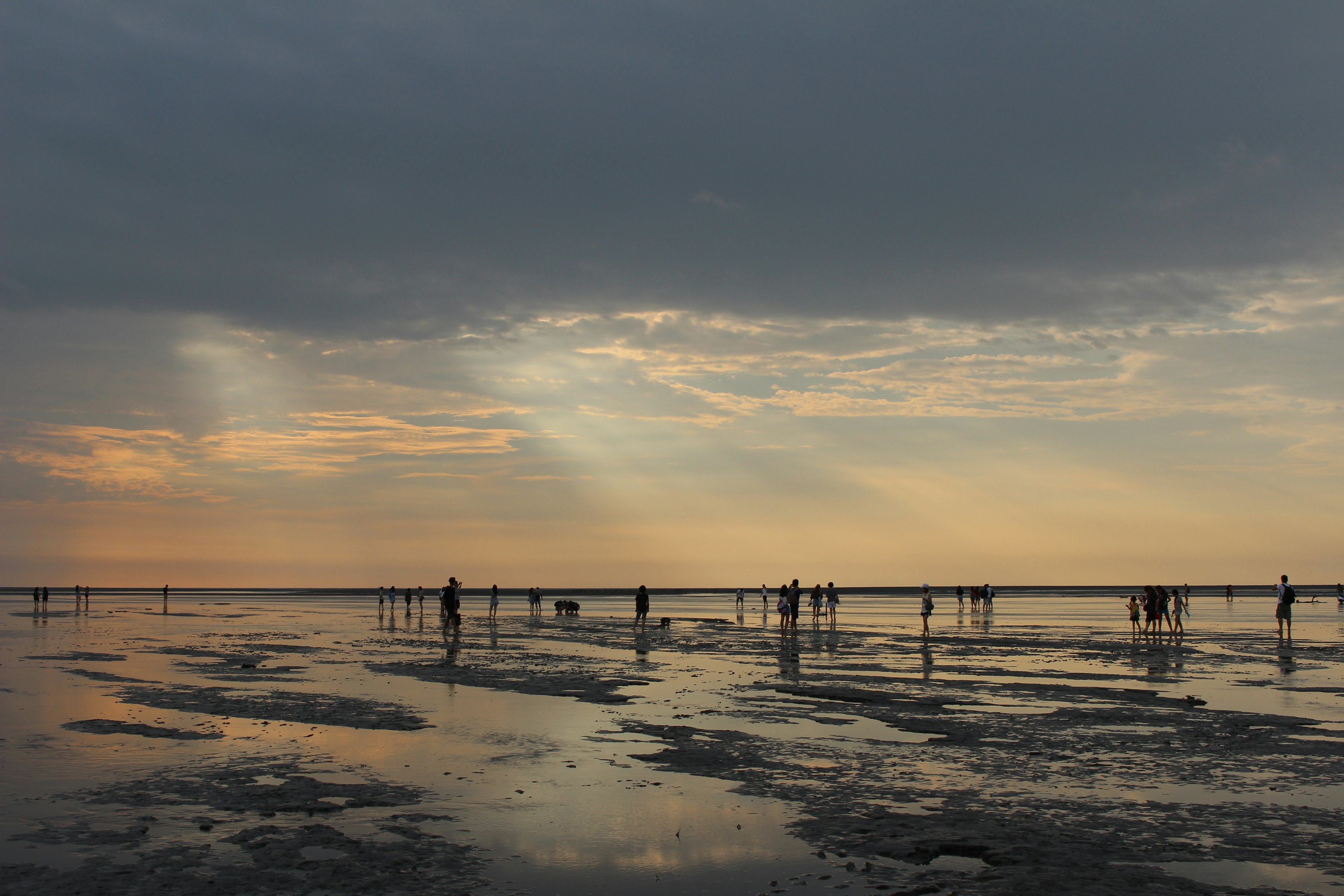 Silhouetten von Personen, die an einem reflektierenden Strand bei Sonnenuntergang spazieren