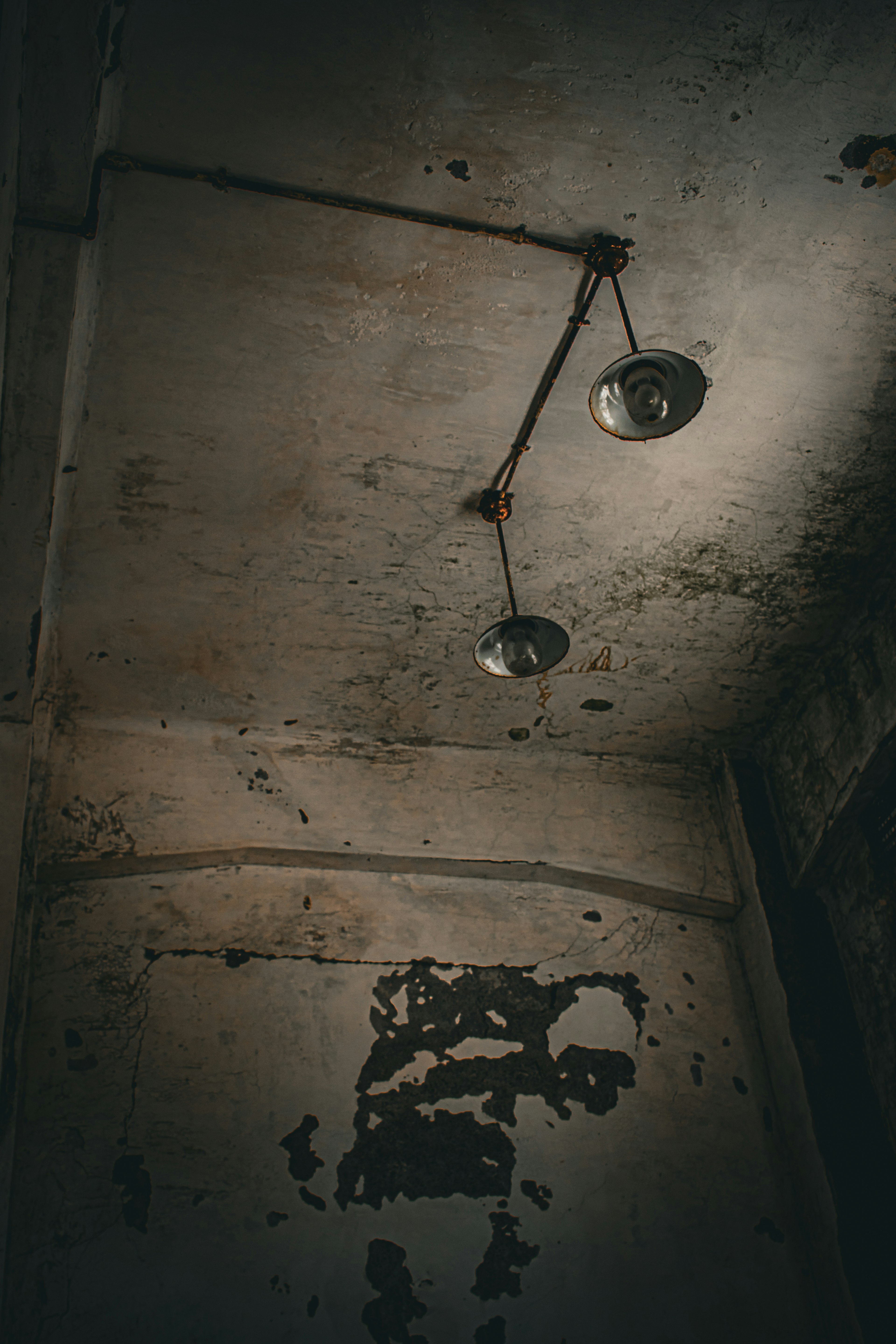 Two vintage light fixtures hanging from the ceiling in a dim room with peeling walls