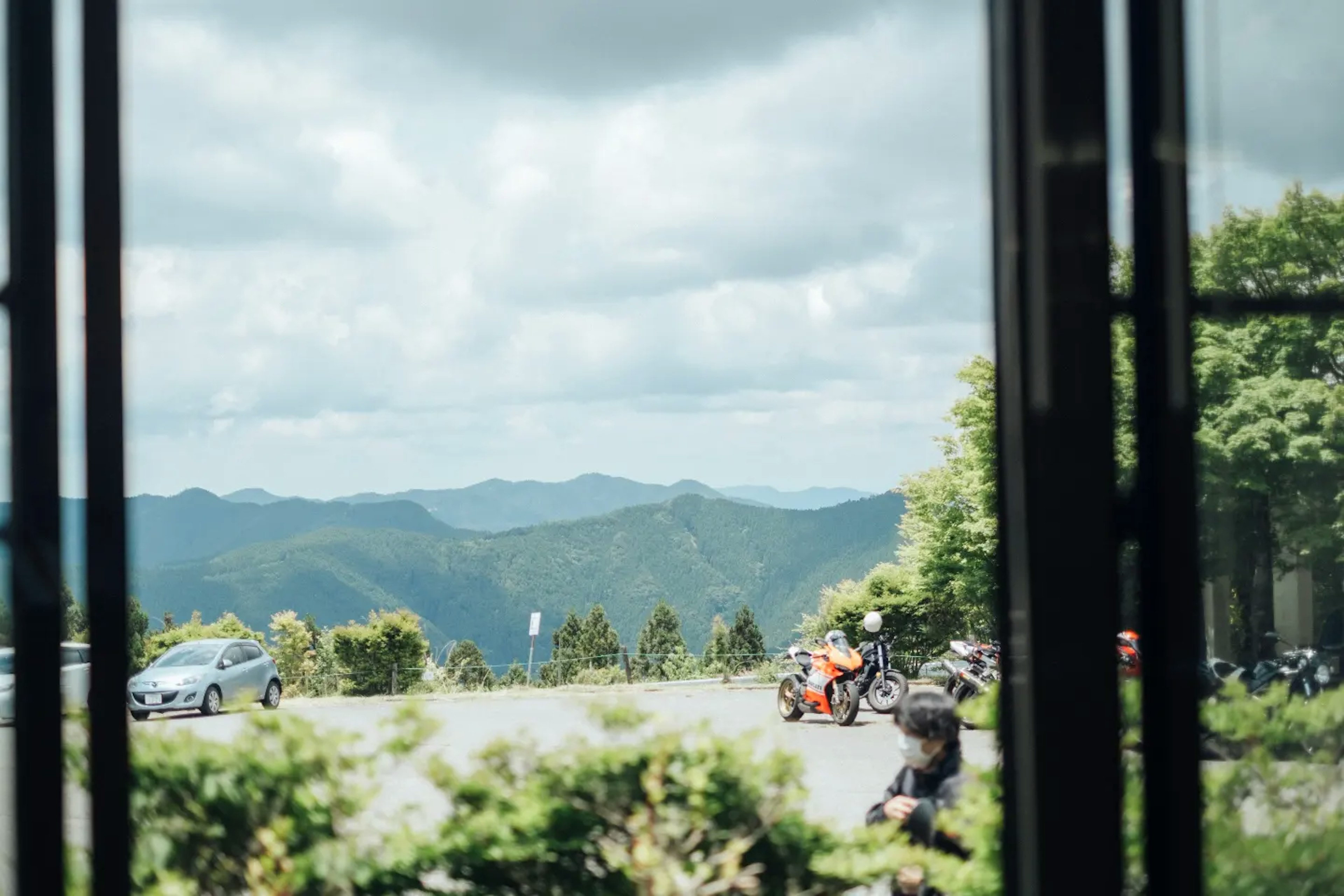 View of mountains and clouds from a window with parked cars and motorcycles