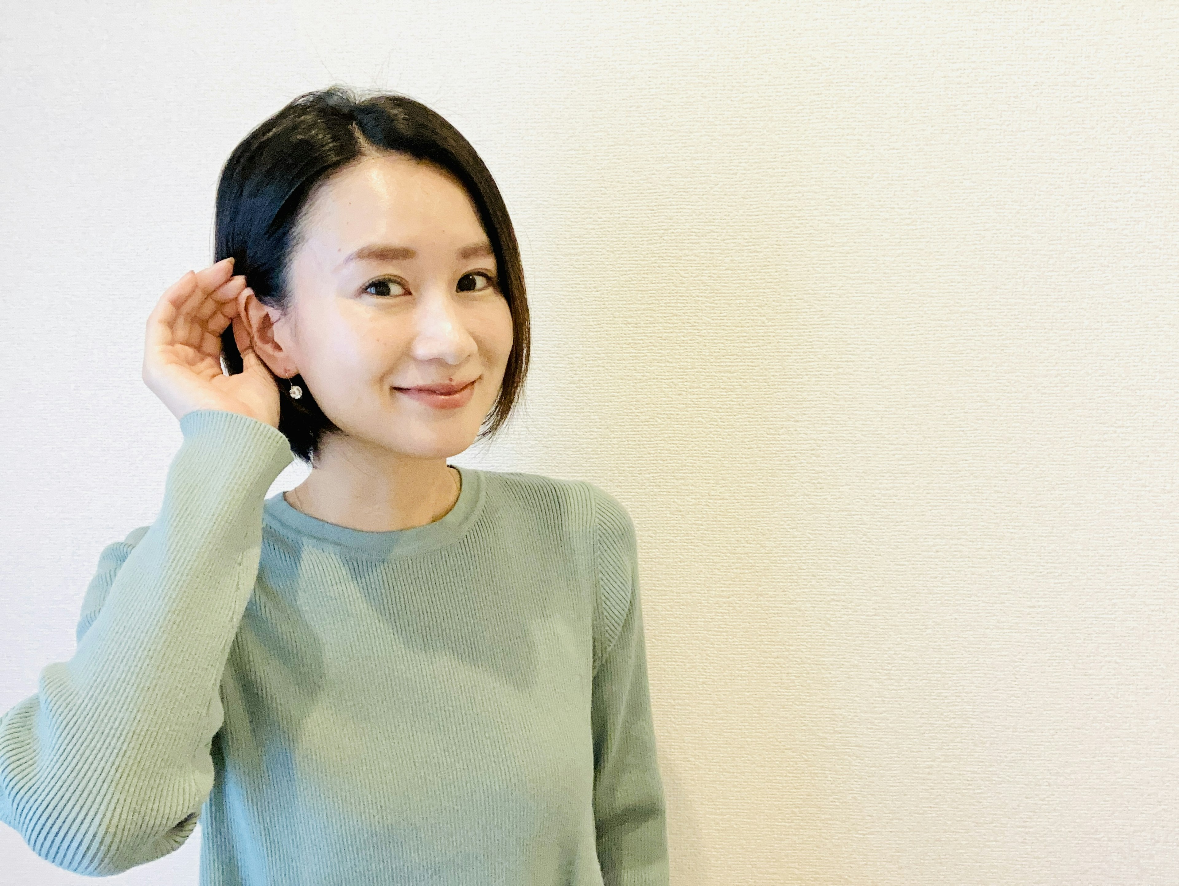 Femme souriante avec la main à l'oreille dans un pull vert clair