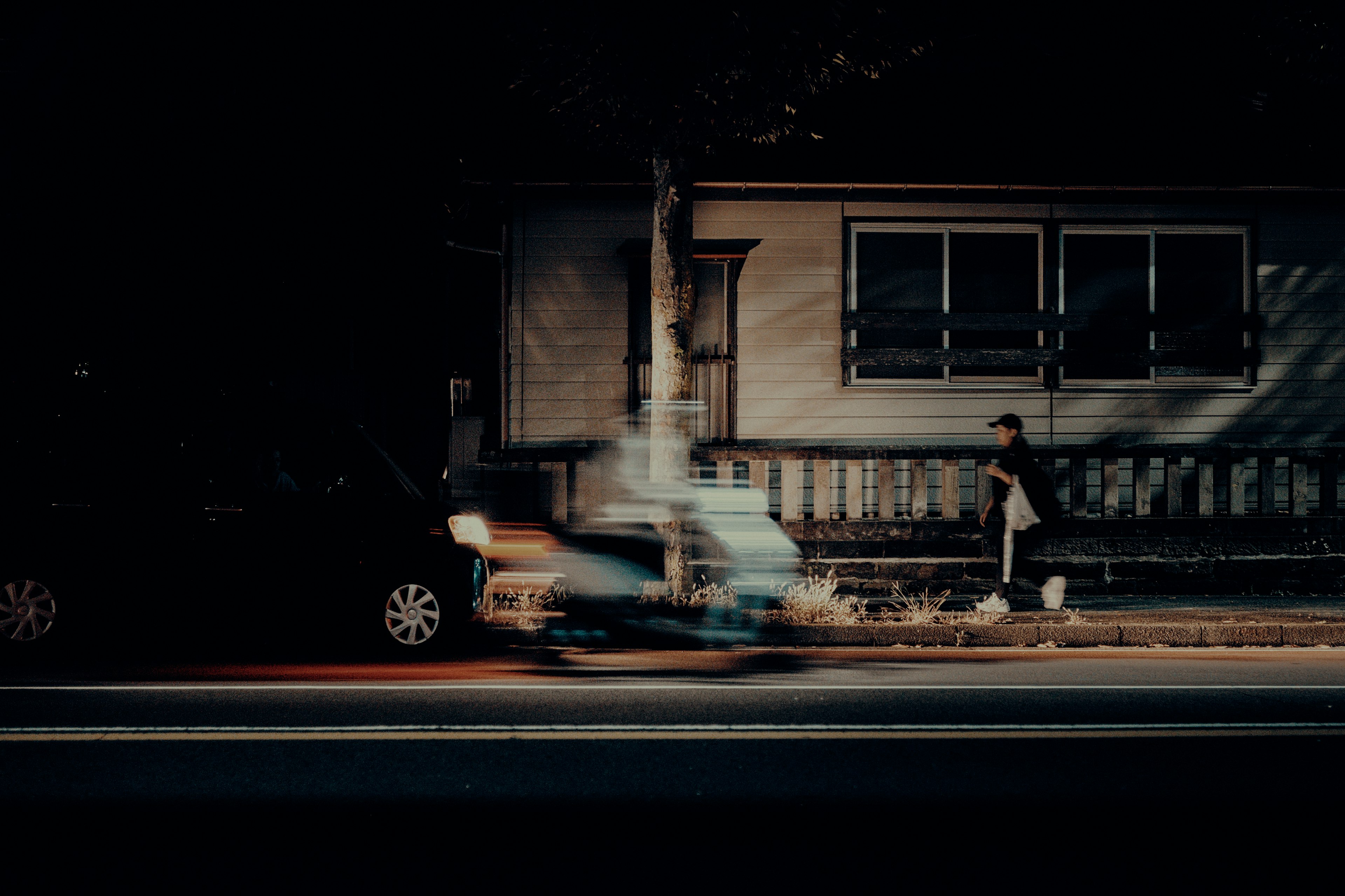 A scene with a blurred car on a dark street and a person walking