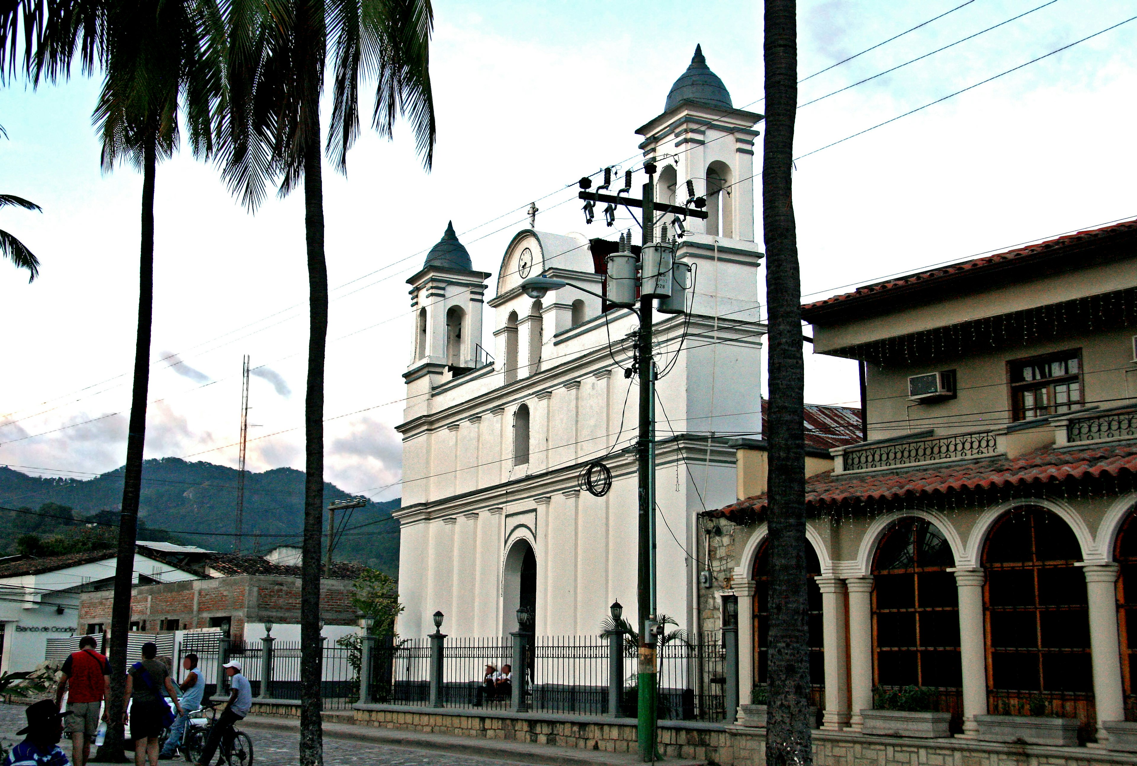 Vue de rue avec une église blanche et des montagnes en arrière-plan