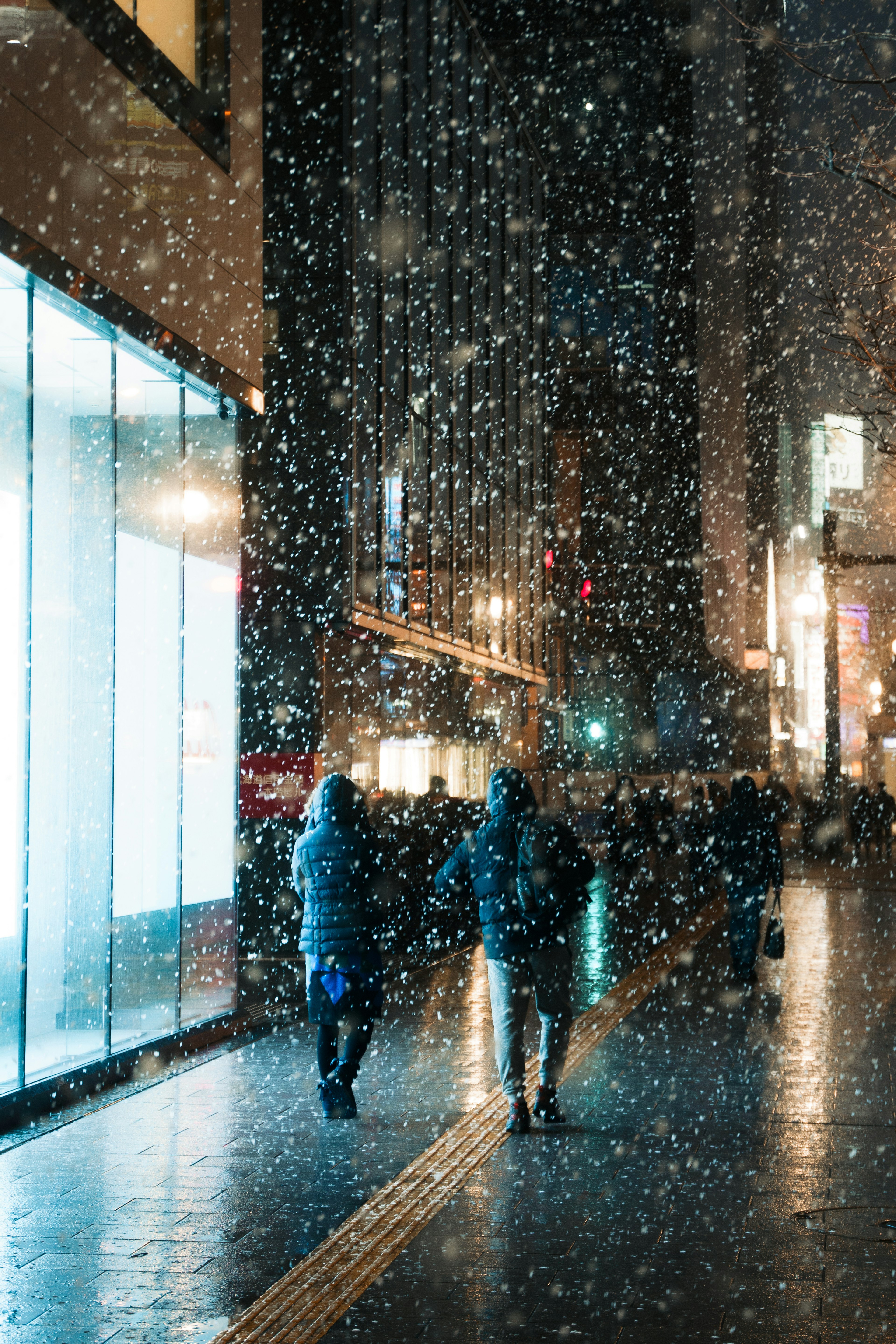 Silhouettes of people walking in a snowy city at night