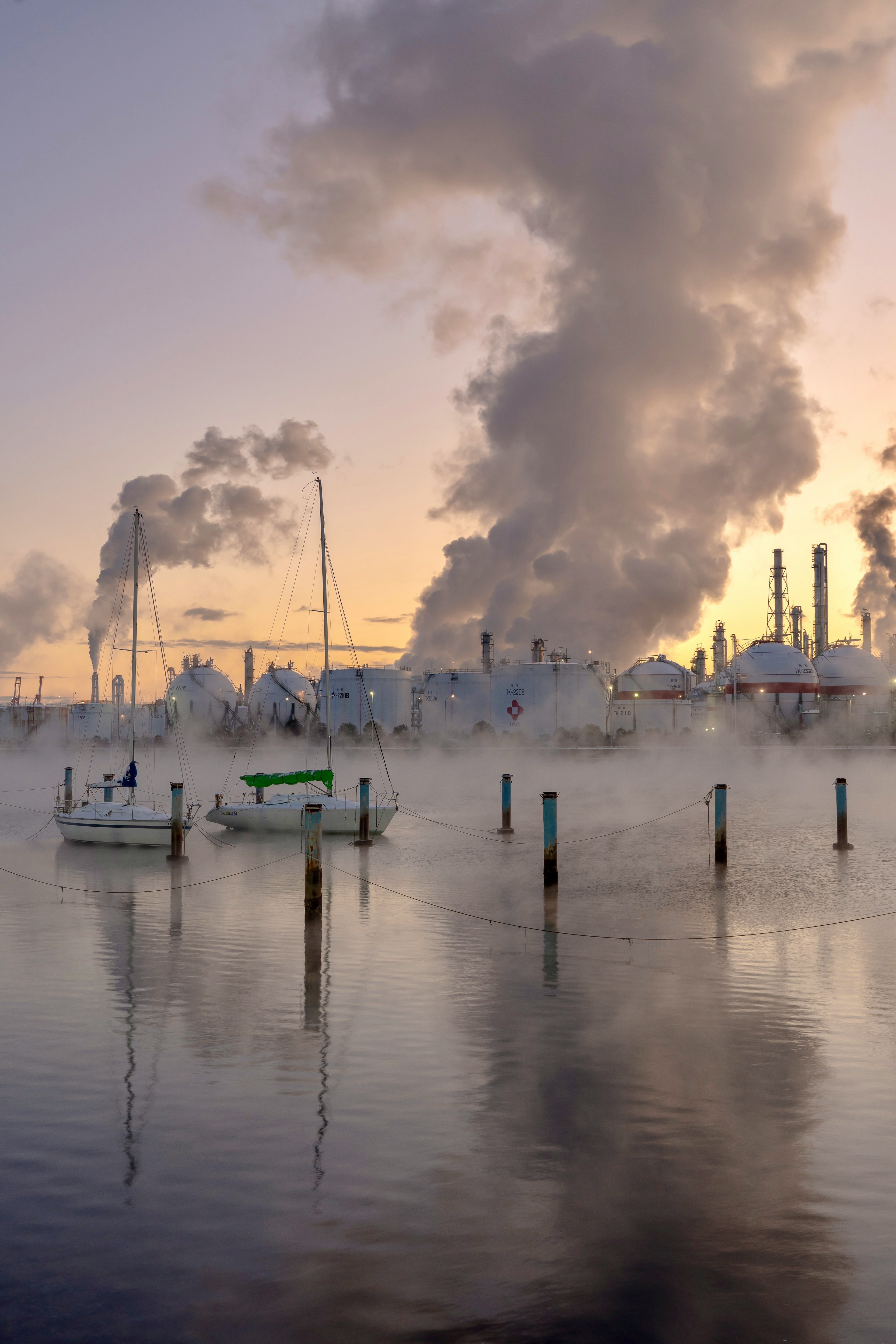 Eine Ansicht von Booten im Nebel mit industriellem Rauch im Hintergrund