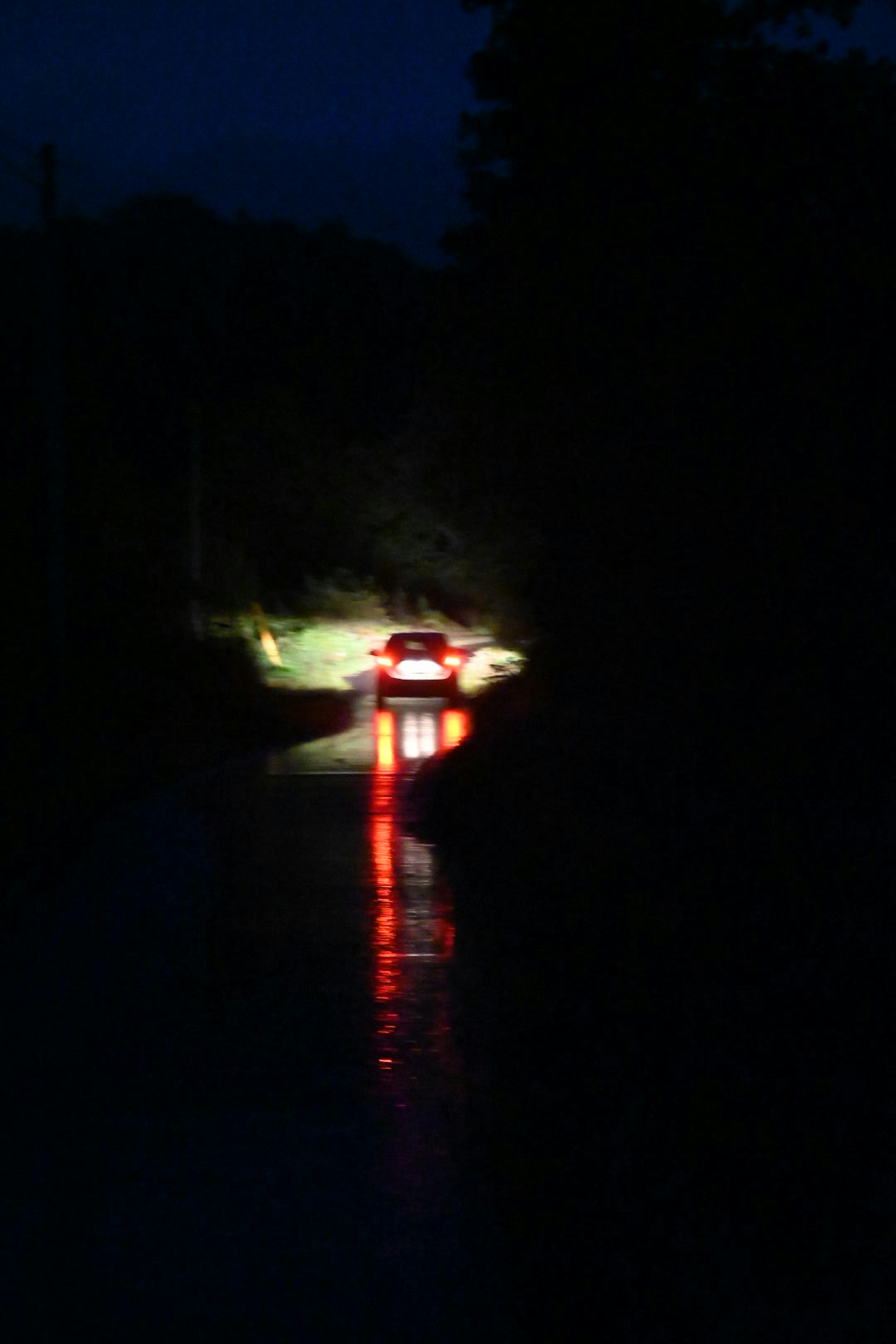 Tampilan belakang mobil di jalan gelap lampu belakang merah dan pantulan di air