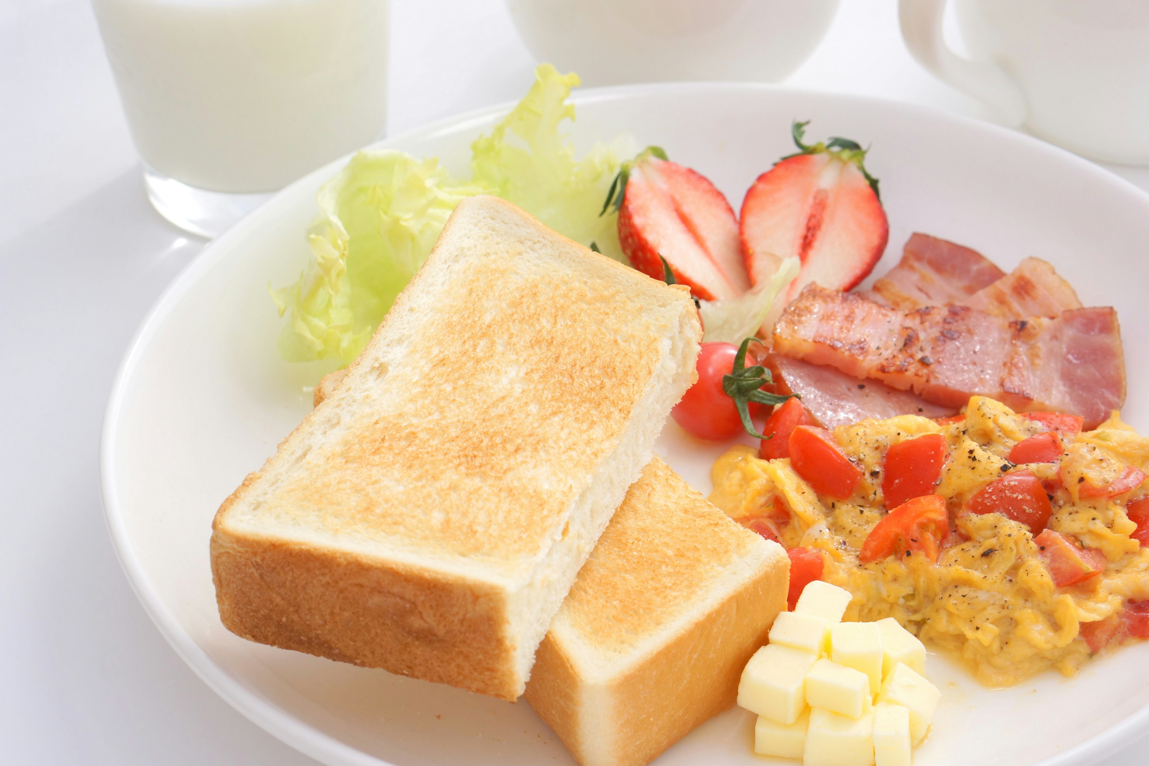 Frühstücksteller mit Toast, Rühreiern, Schinken, Tomaten, Erdbeeren, Salat und Milch