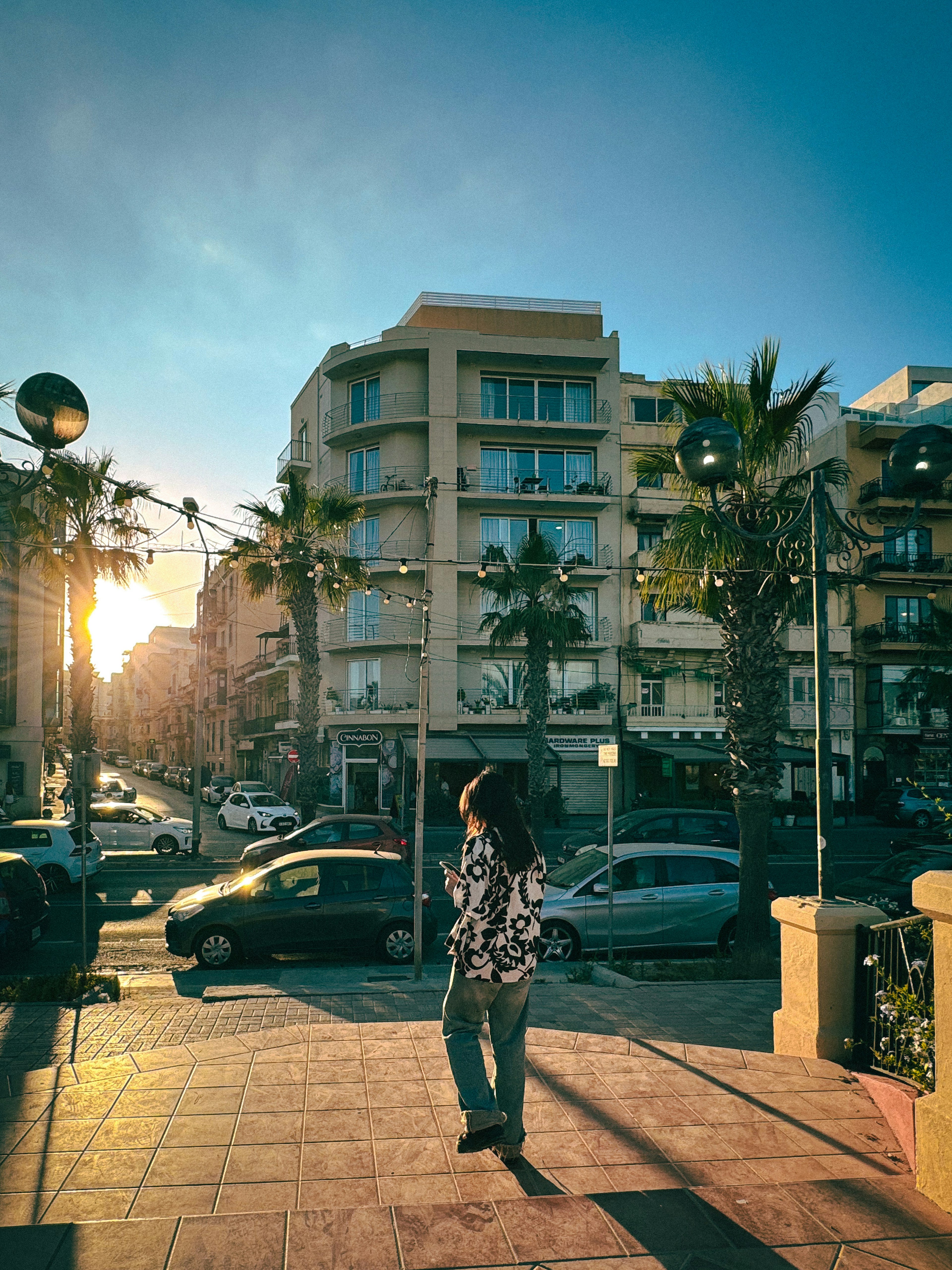 Femme marchant dans la rue avec un coucher de soleil en arrière-plan et des bâtiments