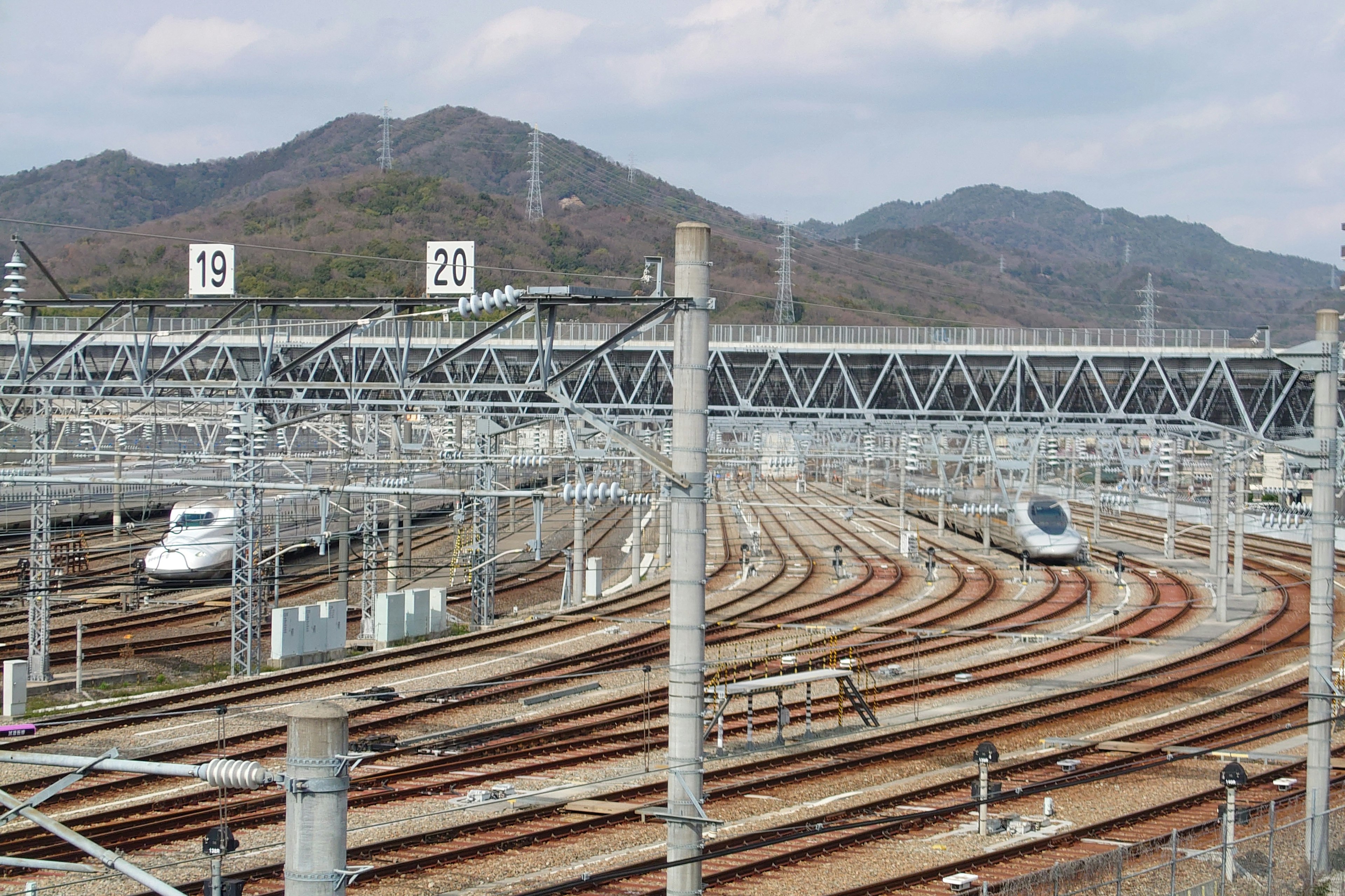 山の背景に新幹線の車両が並ぶ鉄道の風景