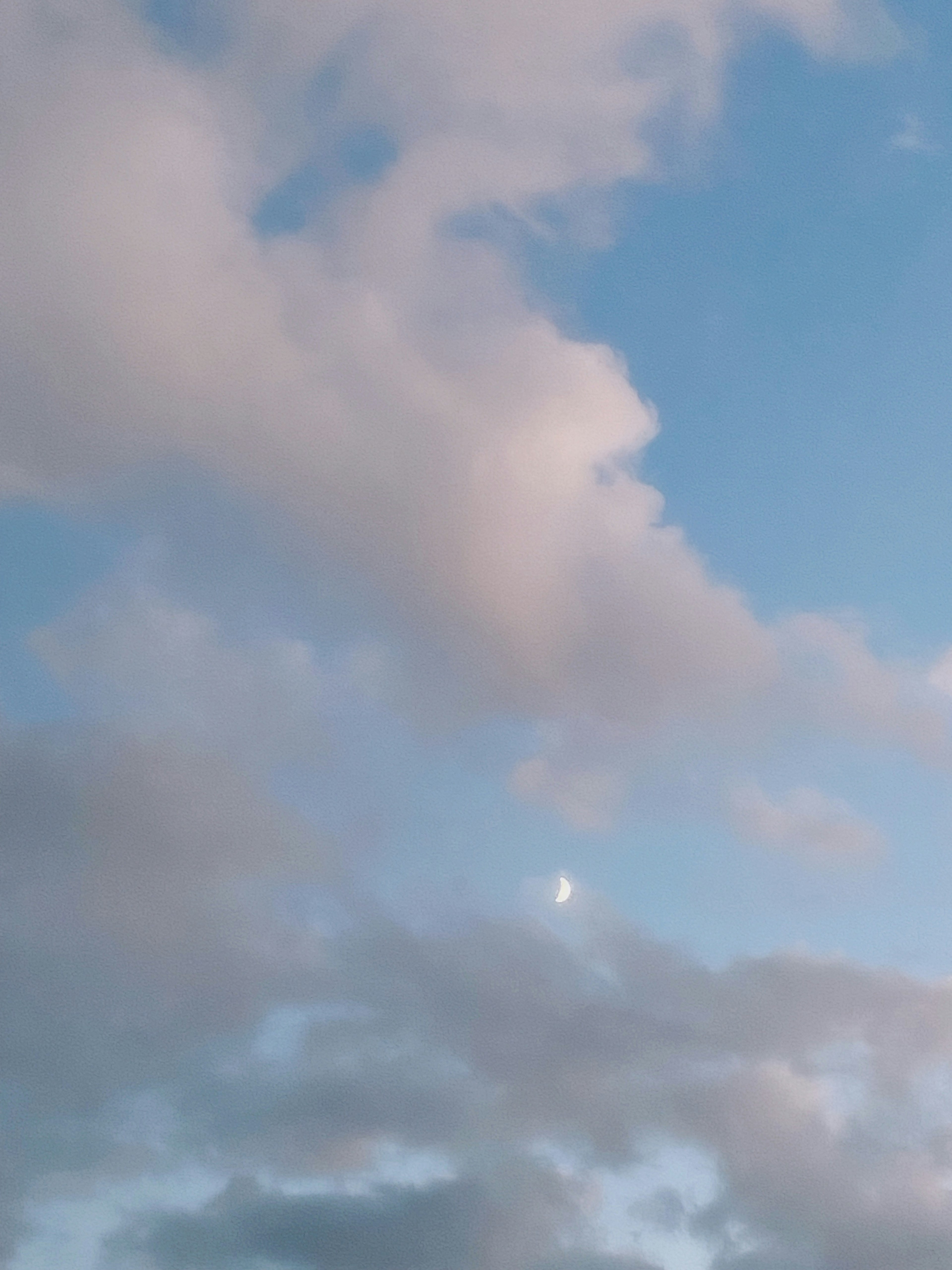 青空に浮かぶ淡い雲と月のシルエット