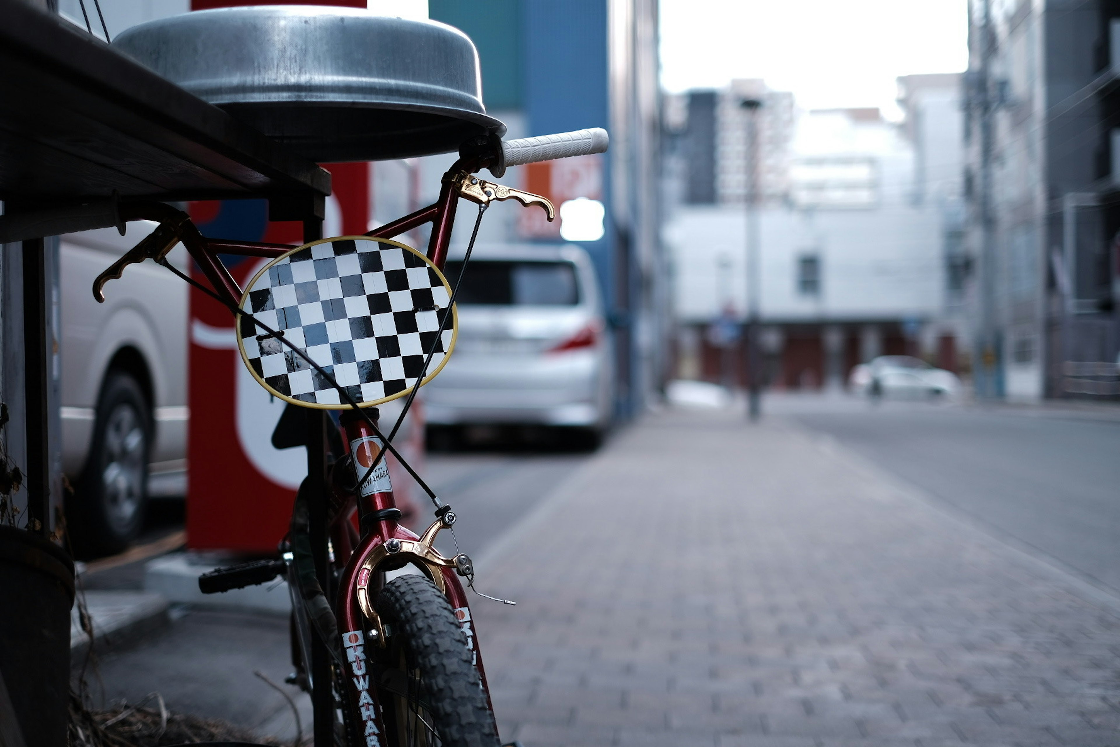 A bicycle parked on the street featuring a checkerboard patterned basket