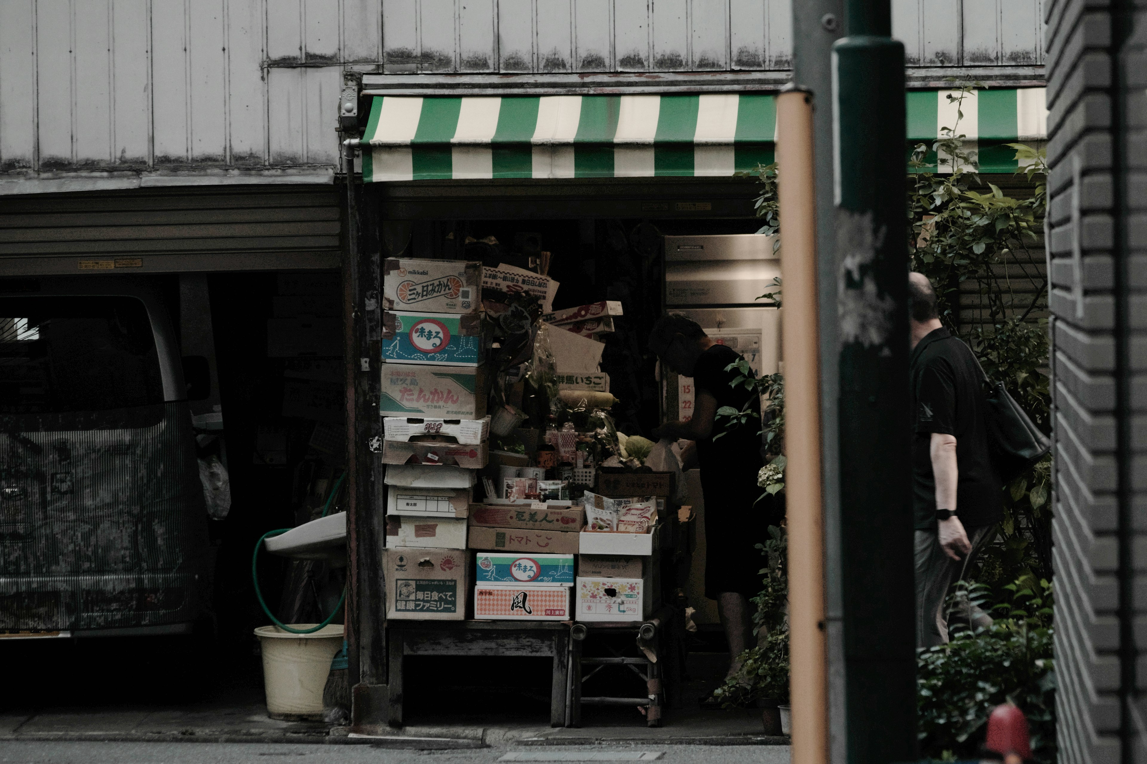 Una entrada de tienda estrecha con cajas de cartón apiladas bajo un toldo a rayas verdes y blancas