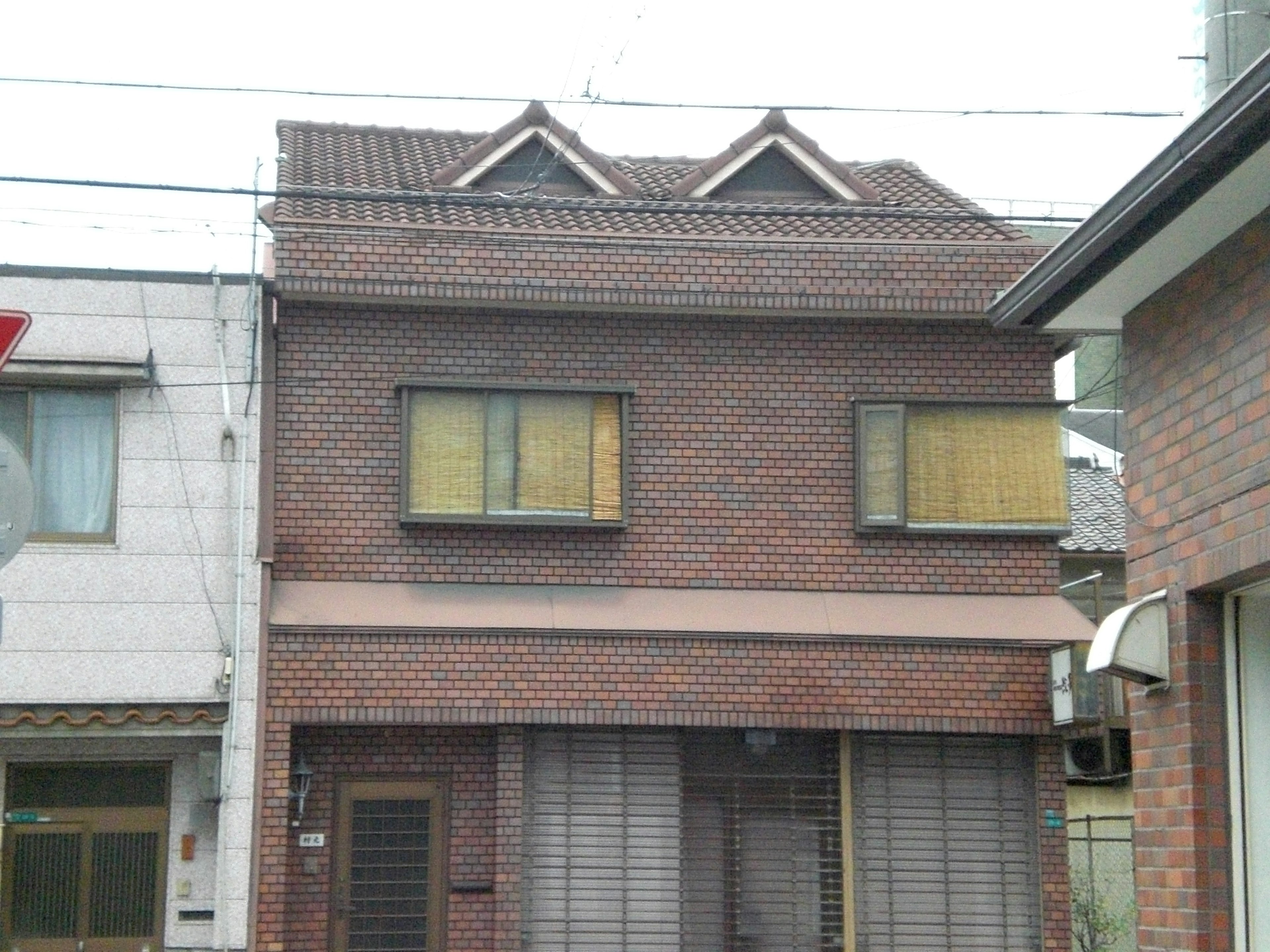 Maison en briques à deux étages avec fenêtres couvertes voisine d'un autre bâtiment