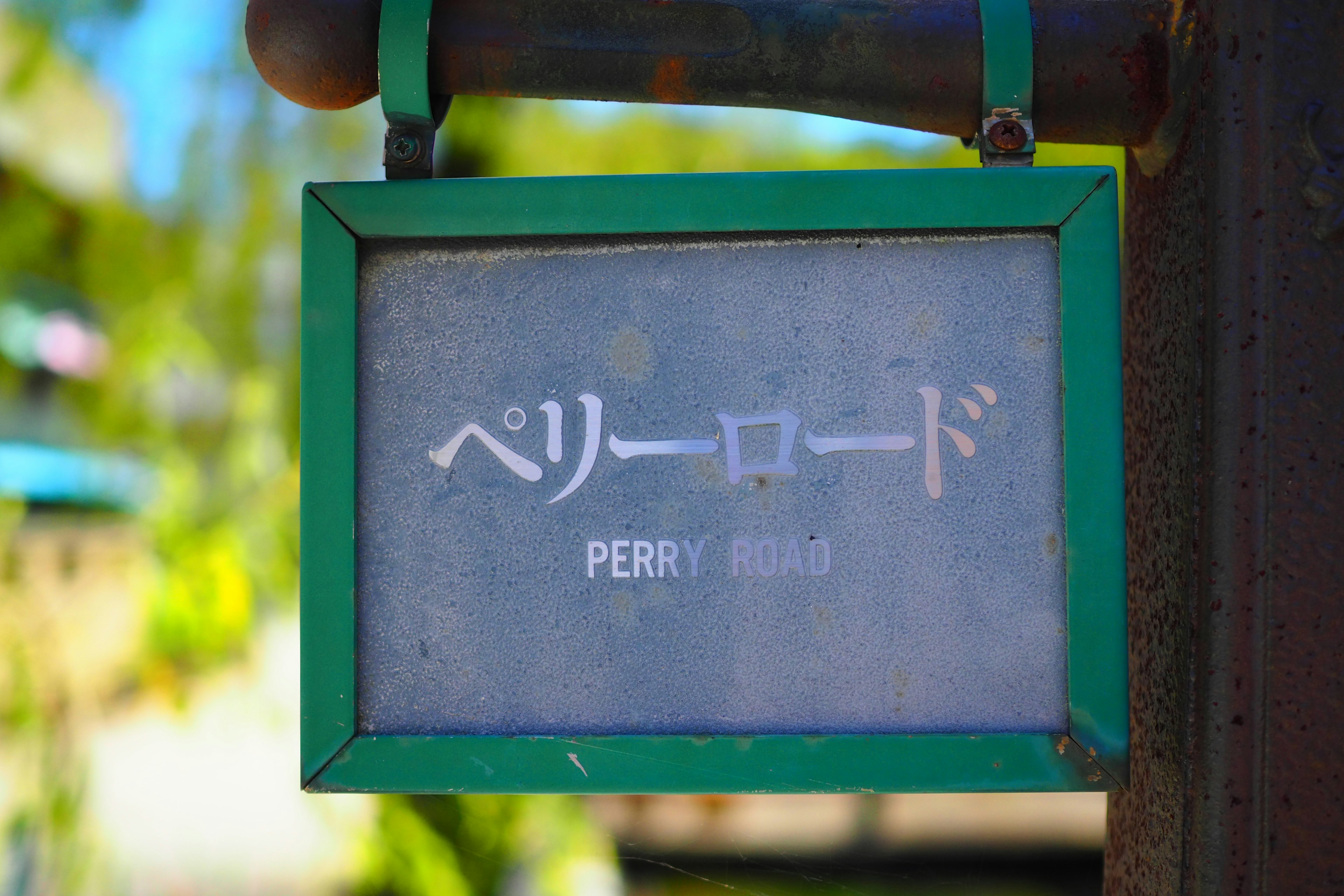 ป้ายที่มีกรอบสีเขียวแสดงข้อความ Perry Road เป็นภาษาญี่ปุ่นและภาษาอังกฤษ