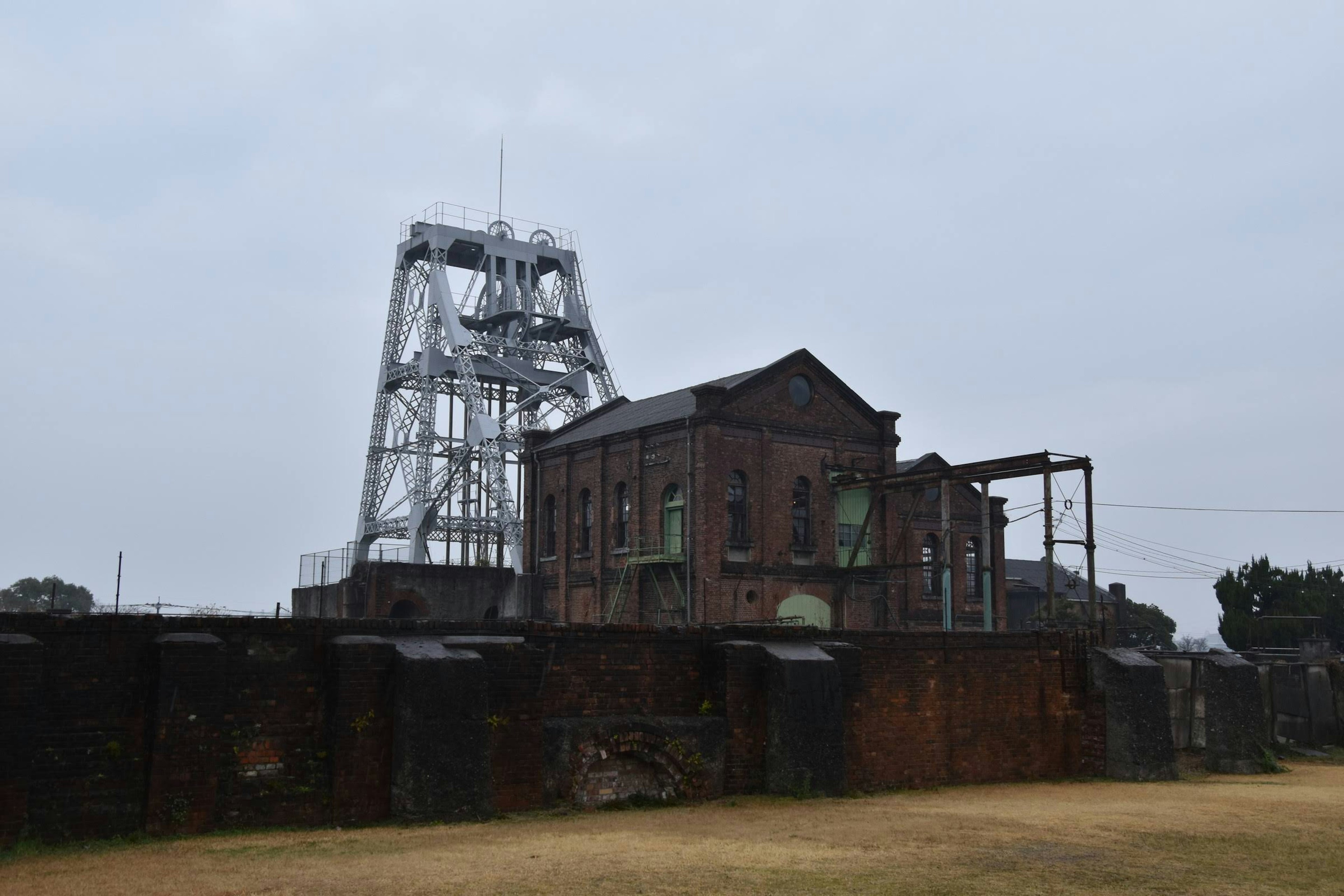 An old mining building and metallic mine shaft stand under a cloudy sky