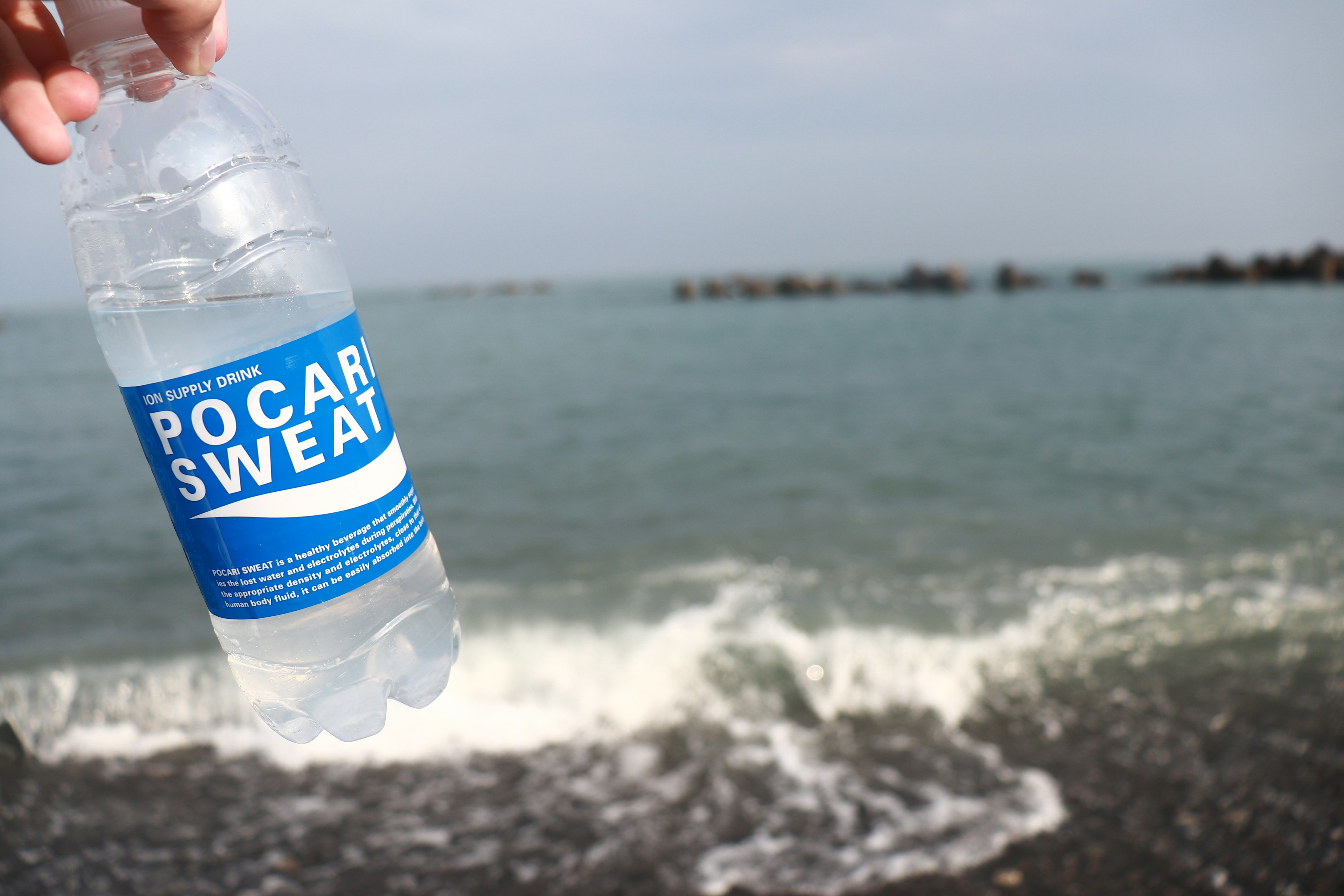 Main tenant une bouteille de Pocari Sweat avec un arrière-plan marin