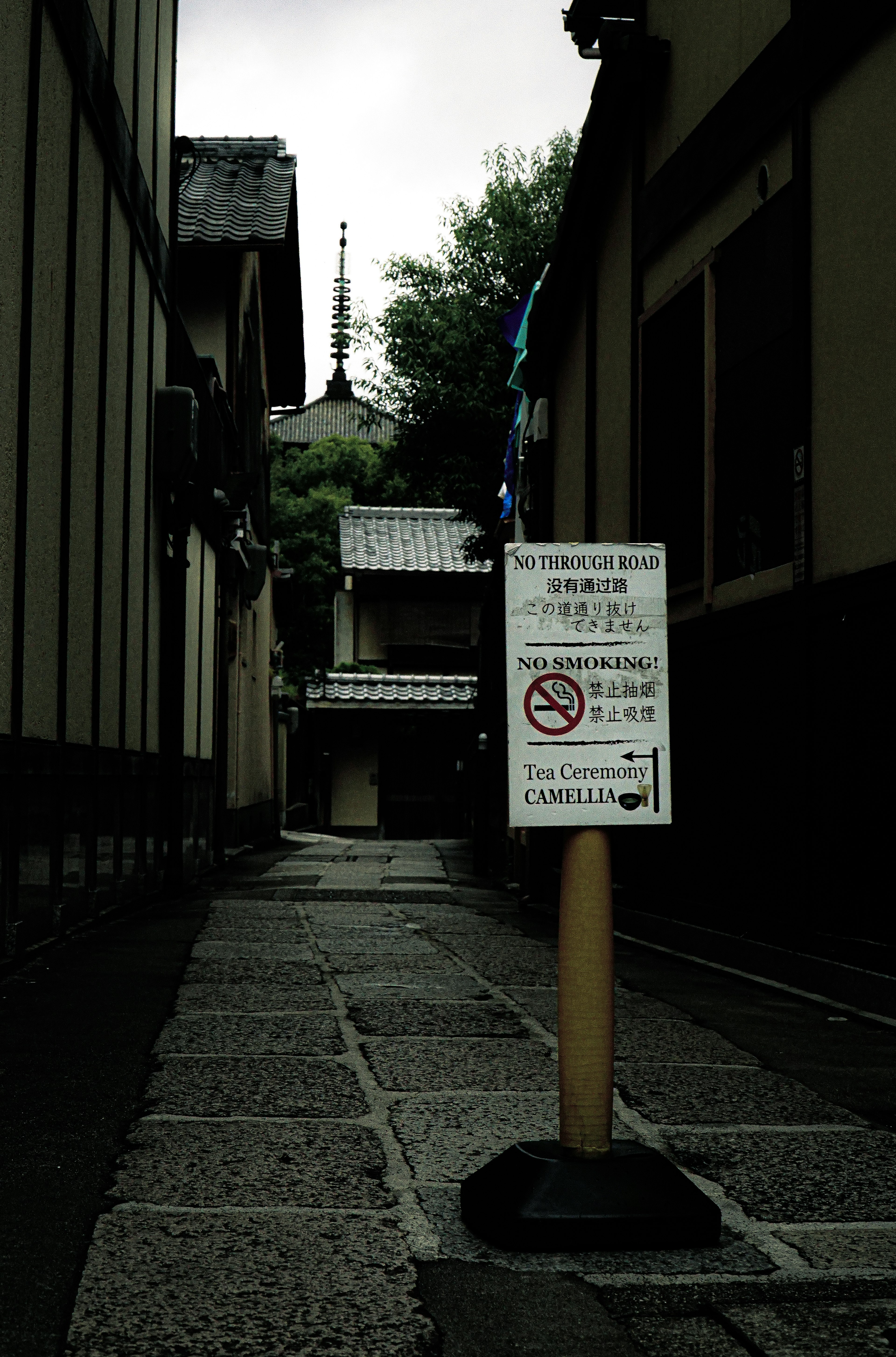 狭い路地に立つ注意看板と周囲の建物が見える風景