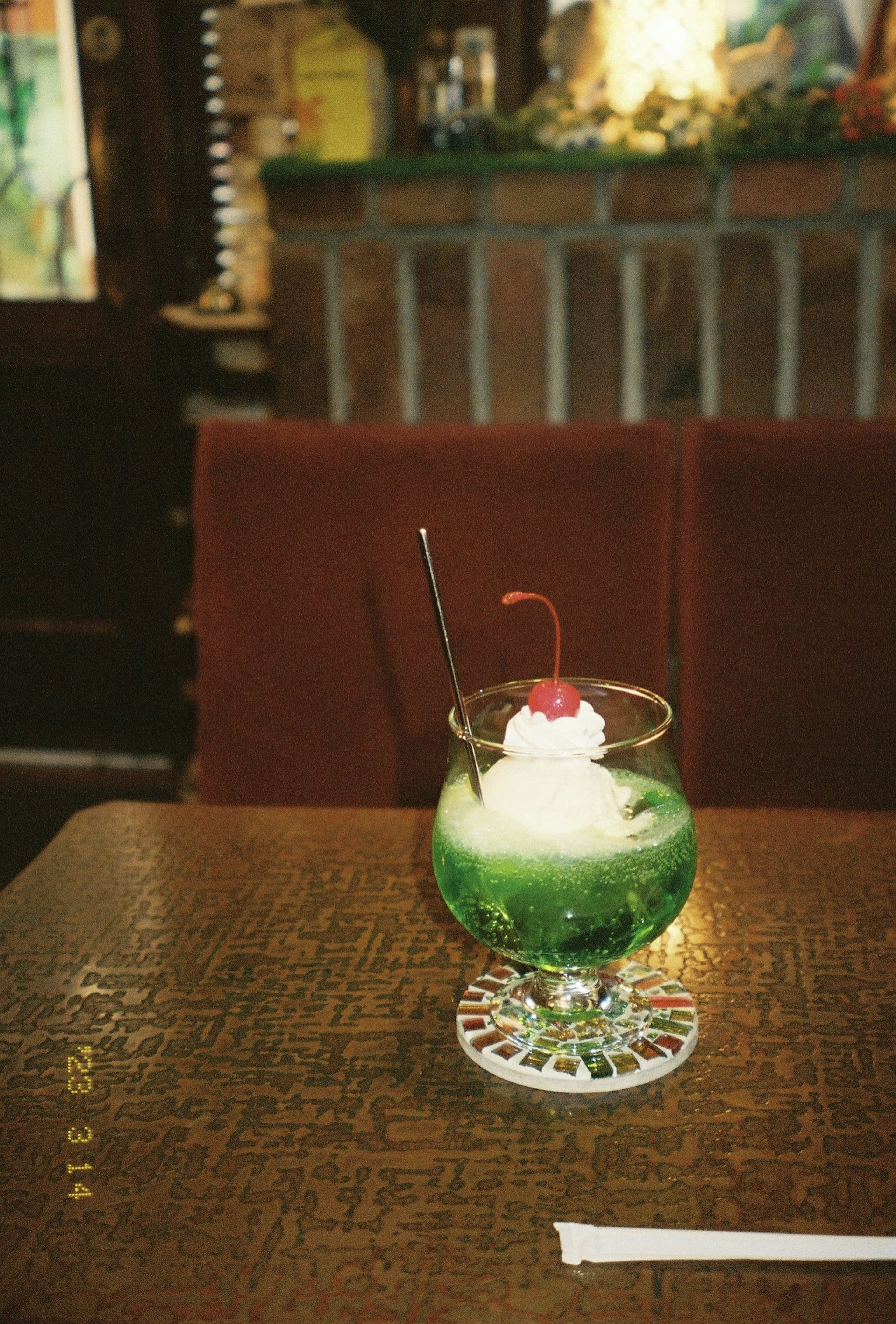 A green drink topped with whipped cream and a cherry served in a decorative glass