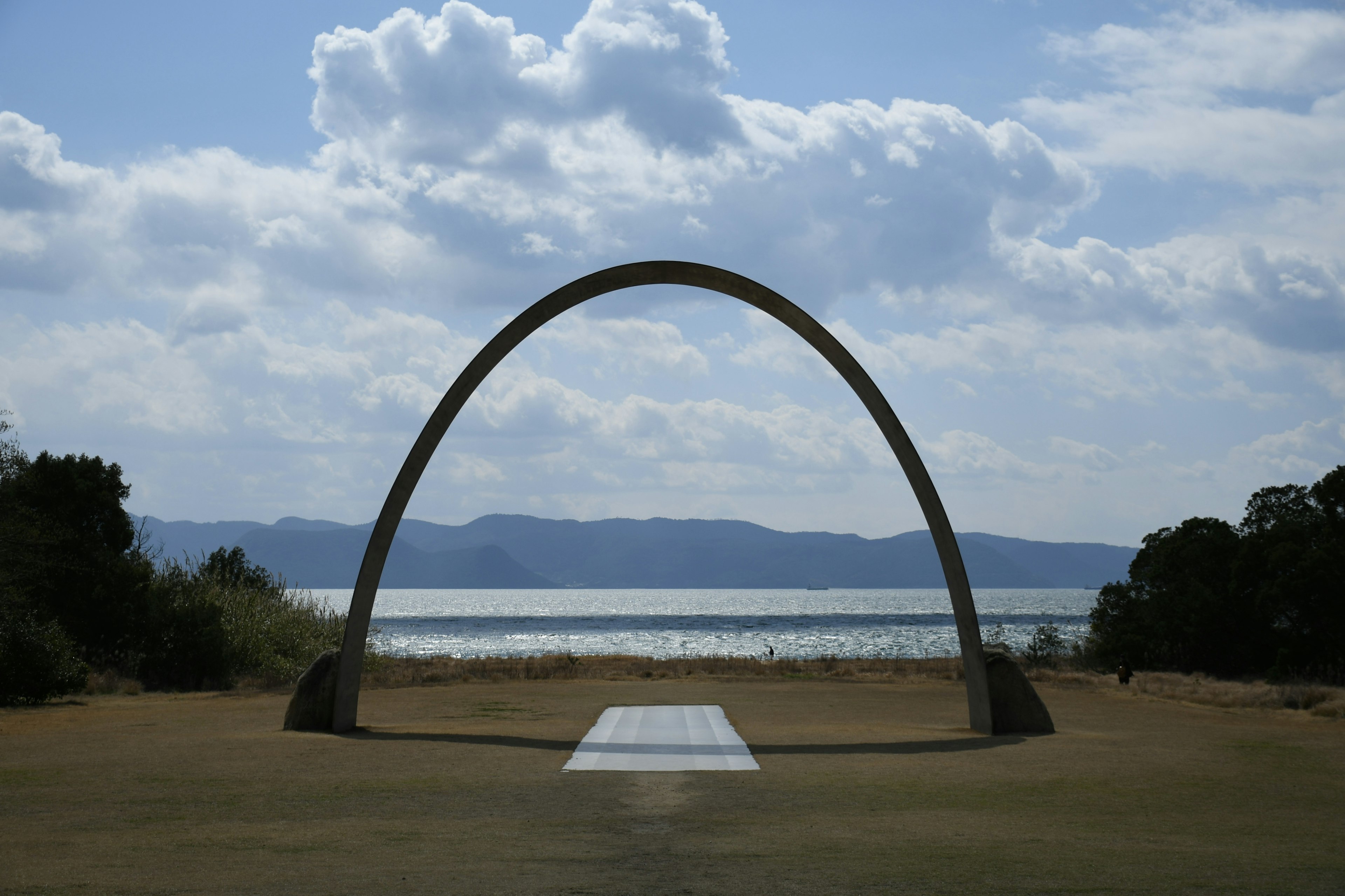 Gran arco metálico bajo un cielo azul con vista al lago