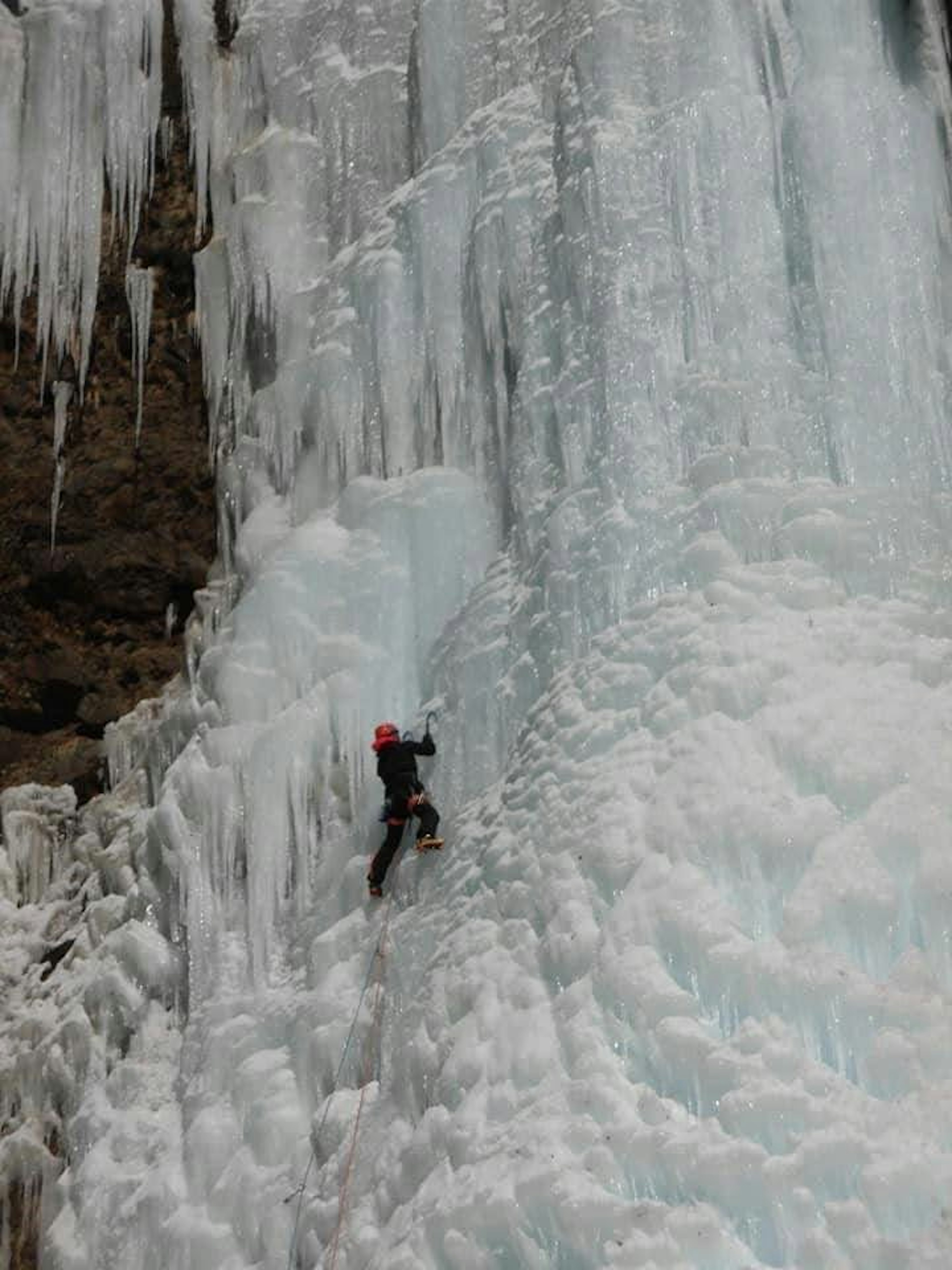 Alpinista che scala una cascata di ghiaccio indossando un casco rosso