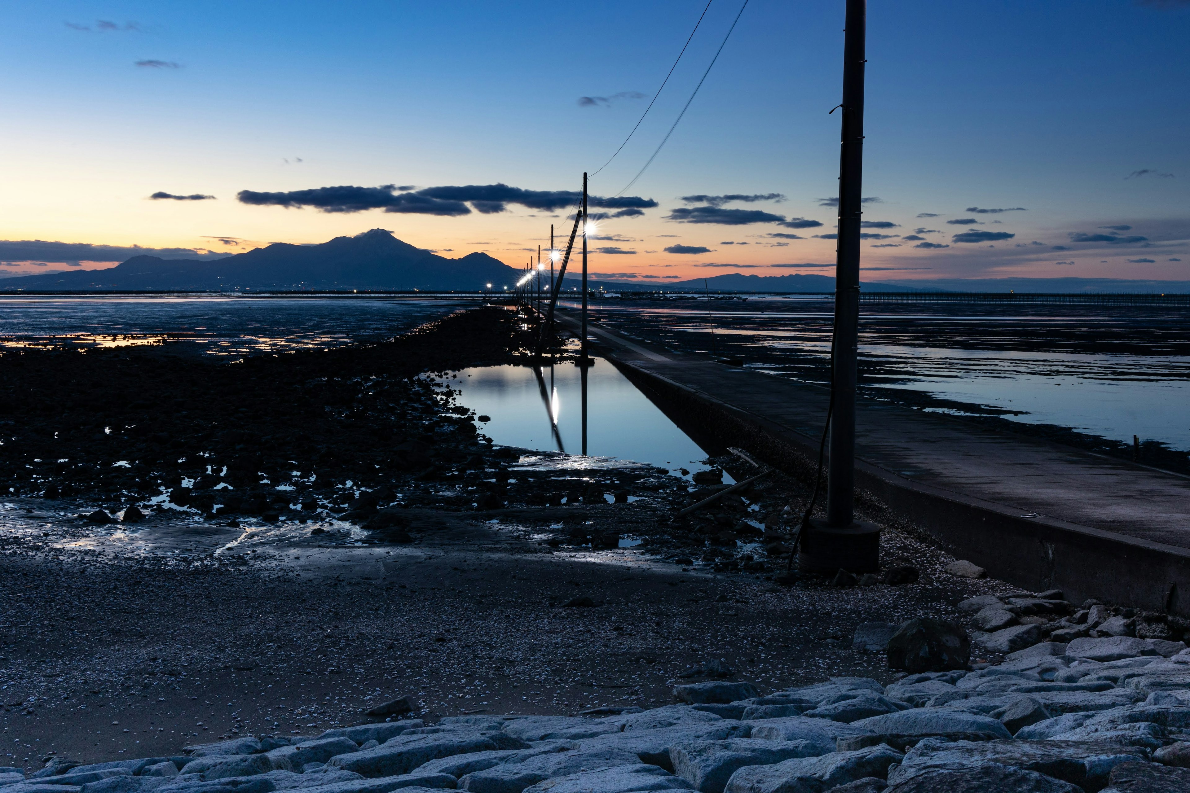 Paysage côtier au crépuscule avec eau calme et montagnes en arrière-plan