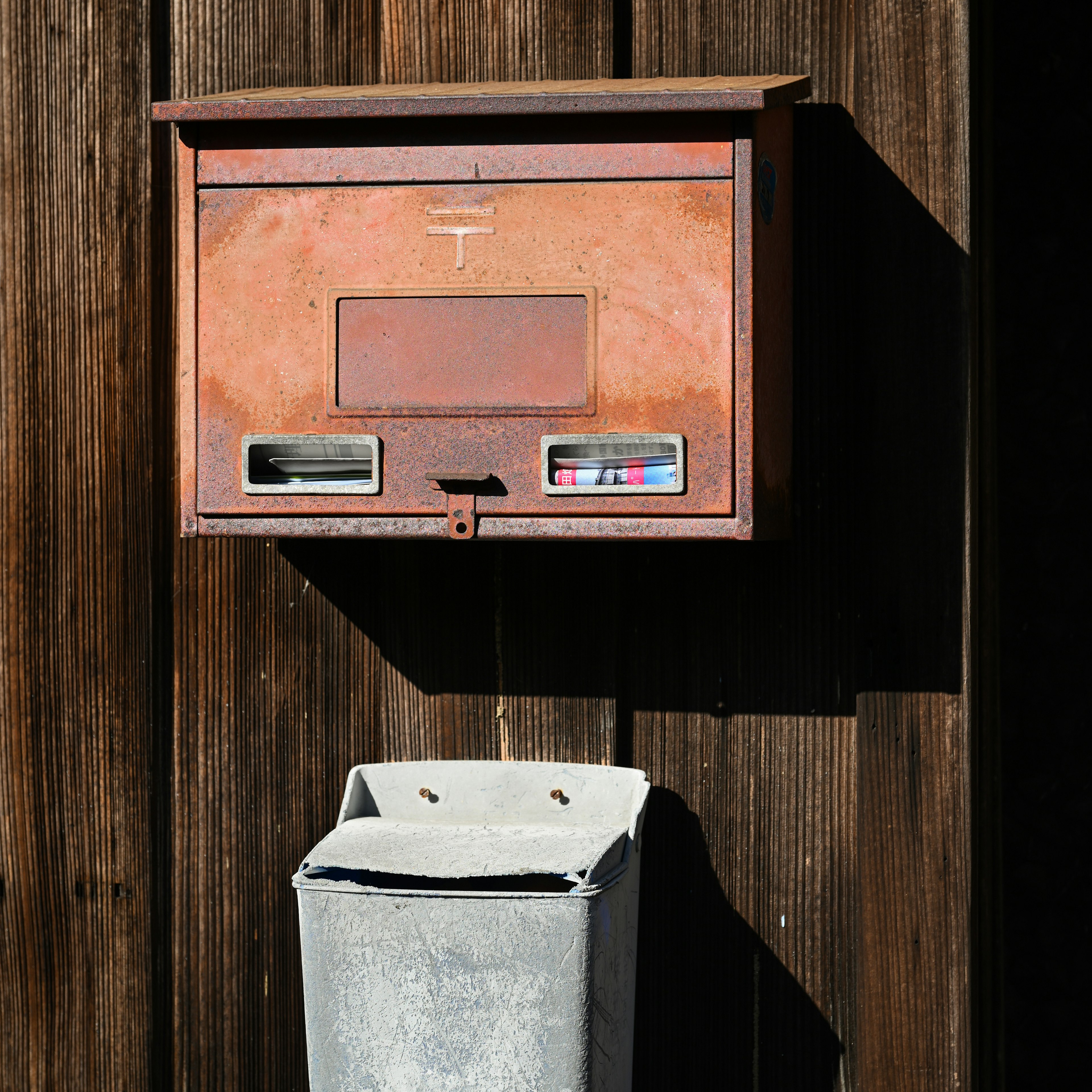 Une vieille boîte aux lettres et une poubelle fixées sur un mur en bois