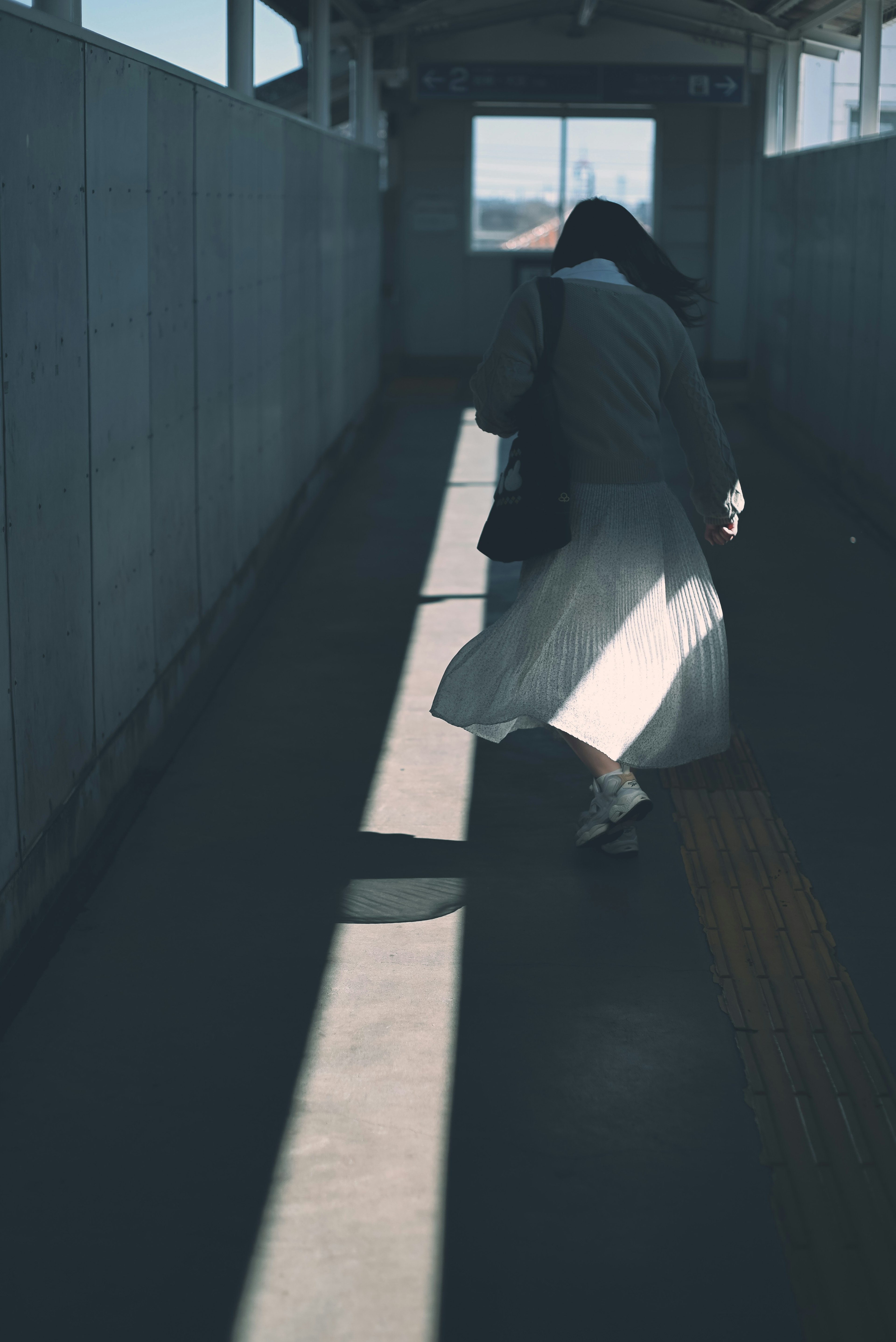 A woman walking through a corridor with light and shadow contrasts