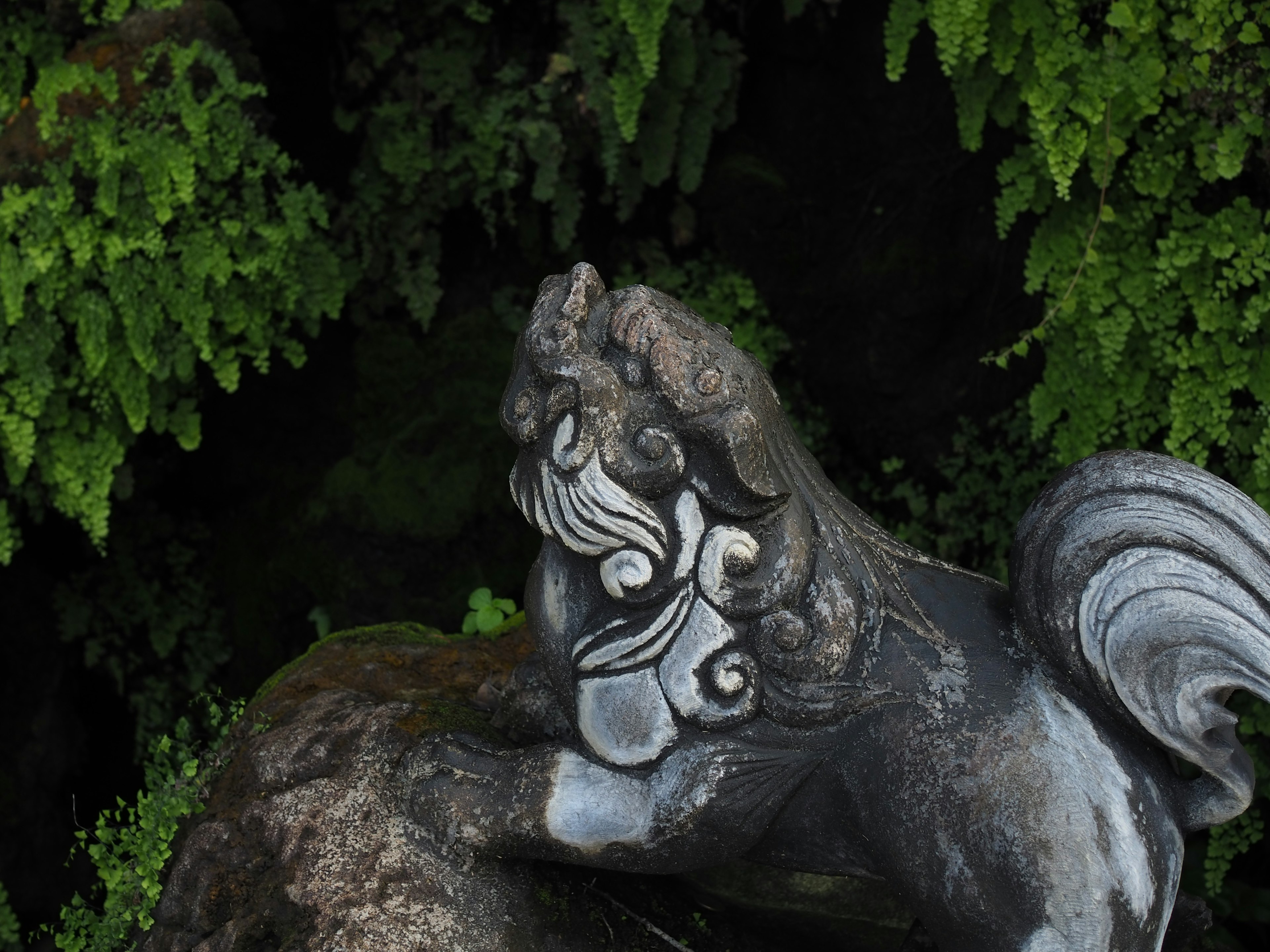 Side view of a stone lion statue against a green background