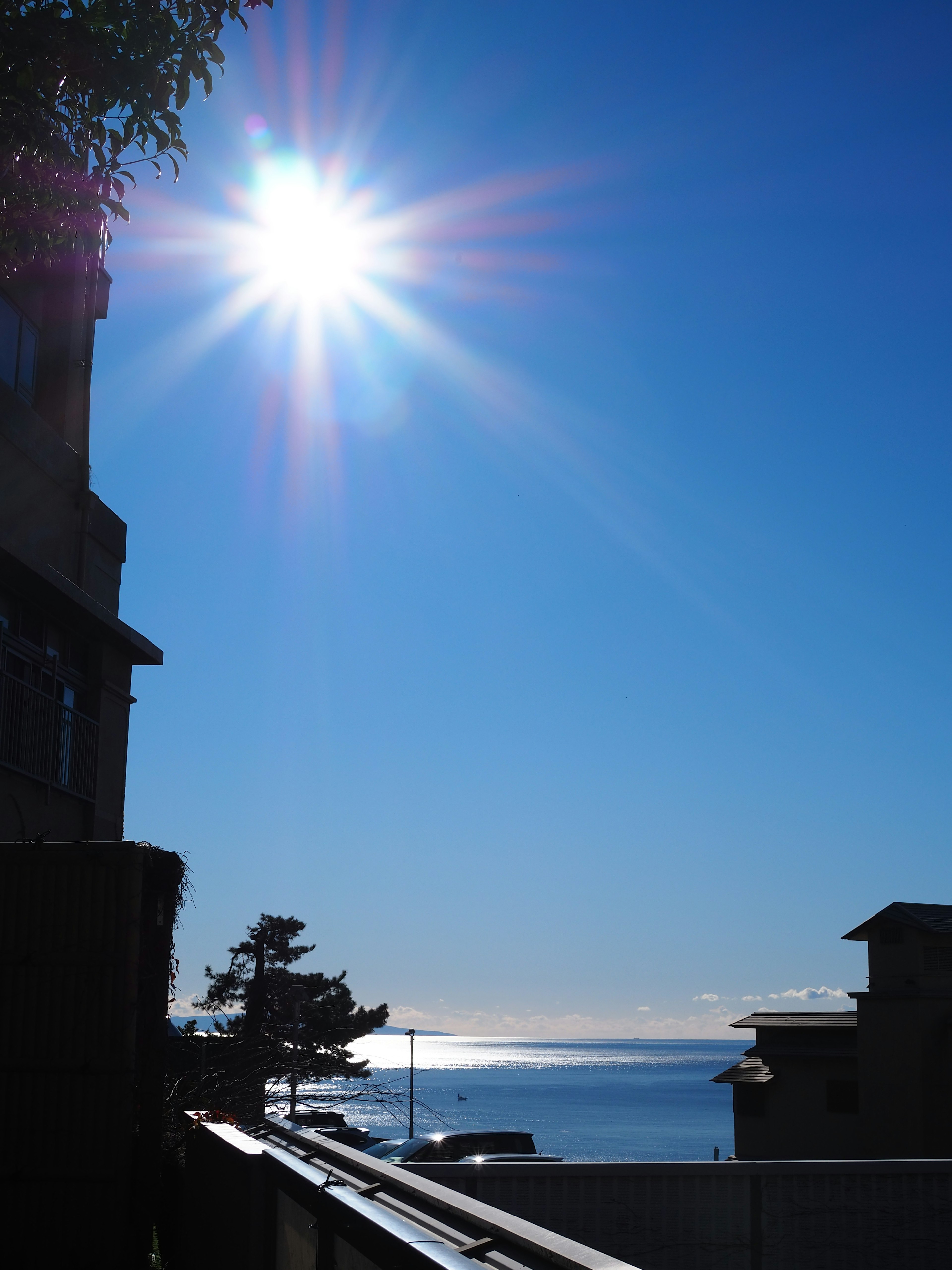 Bright sun shining over a clear blue sky with silhouettes of buildings and ocean view